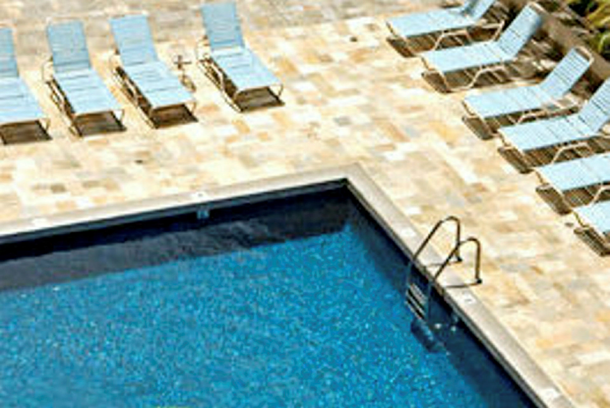 Bild på en klarblå pool med solstolar placerade på en stenlagd yta runt omkring. (AI-genererad text)