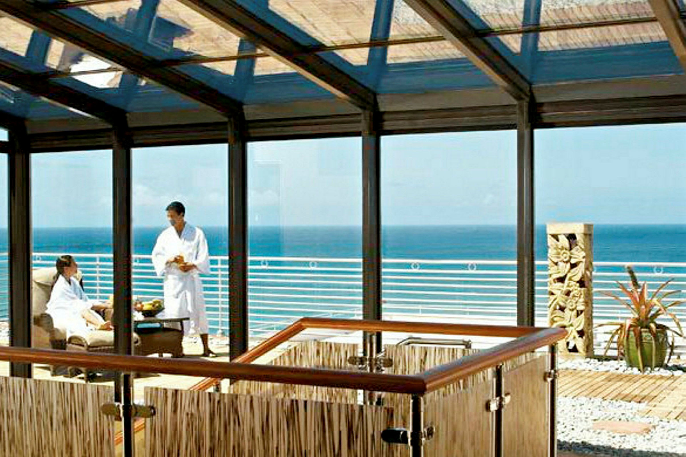 En inglasad lounge med utsikt över havet och en terrass som inkluderar en skulptur och växter. (AI-genererad text)