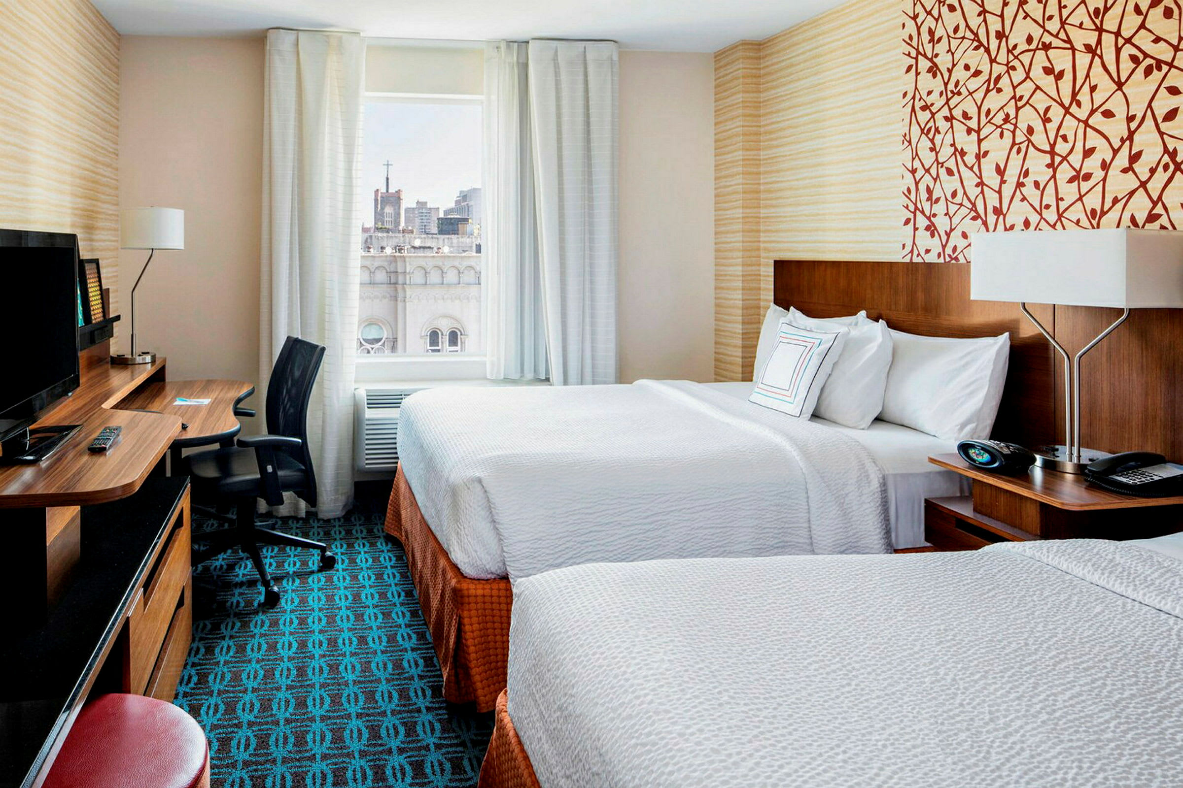 Ett hotellrum med två sängar, ett skrivbord bredvid en stol och ett fönster med stadsvy. (AI-genererad text)