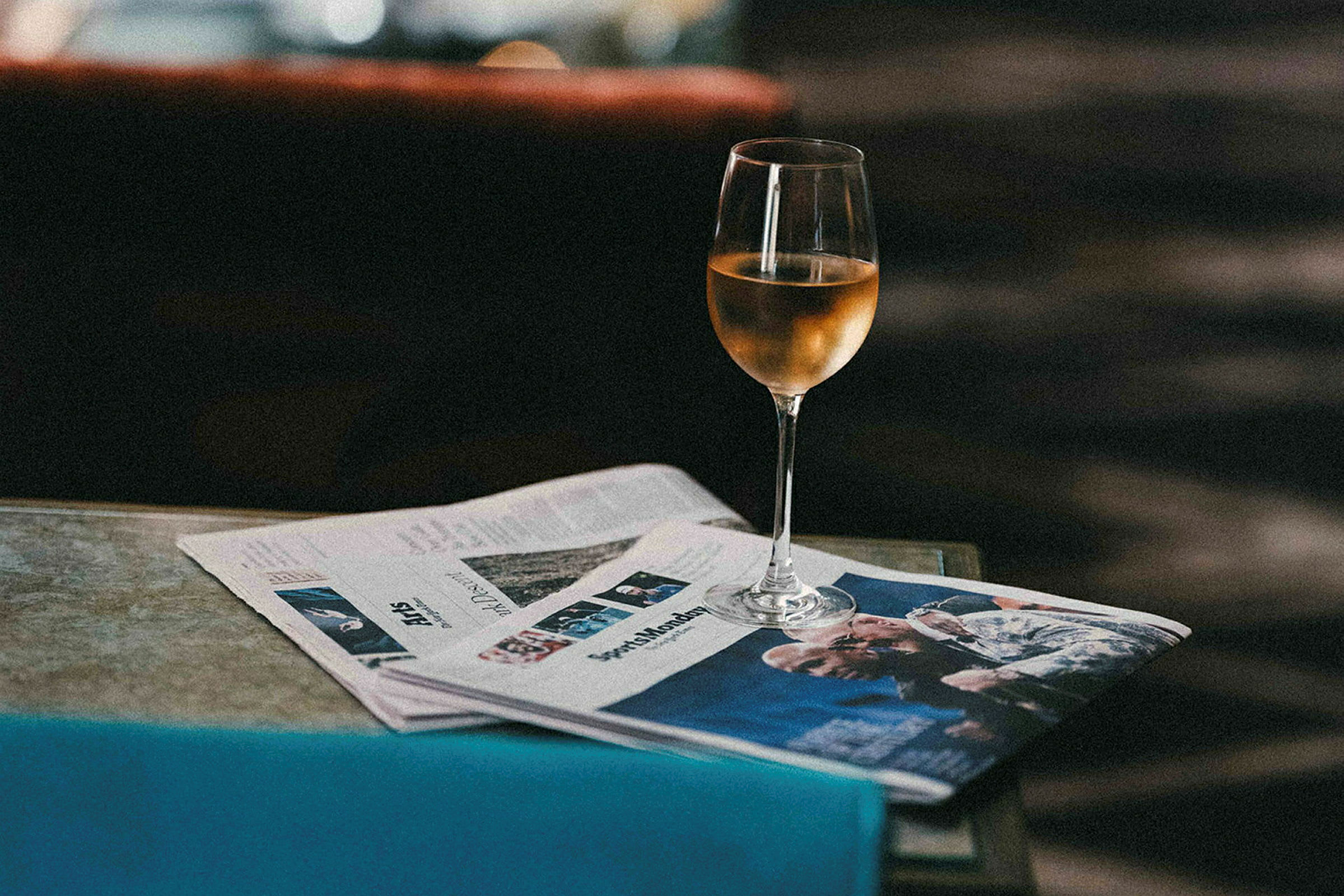 Ett glas vitvin står på ett bord bredvid en tidning. (AI-genererad text)