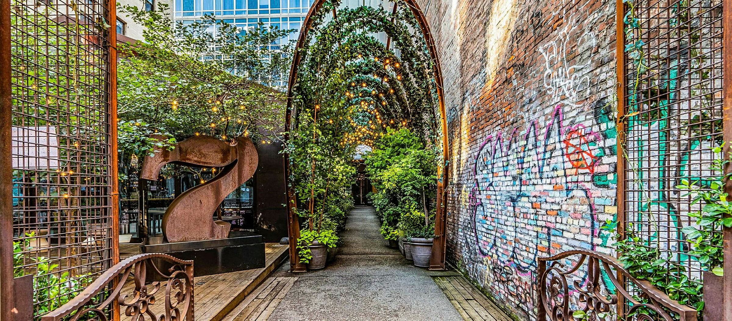 En gränd med en täckt gång och växter samt tegelvägg märkt med graffiti. (AI-genererad text)