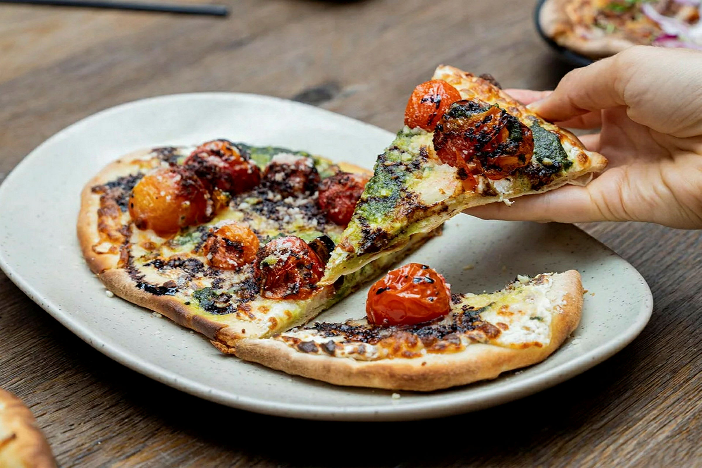 En tallrik med en pizza toppad med rostade tomater och pesto, där någon tar en bit. (AI-genererad text)