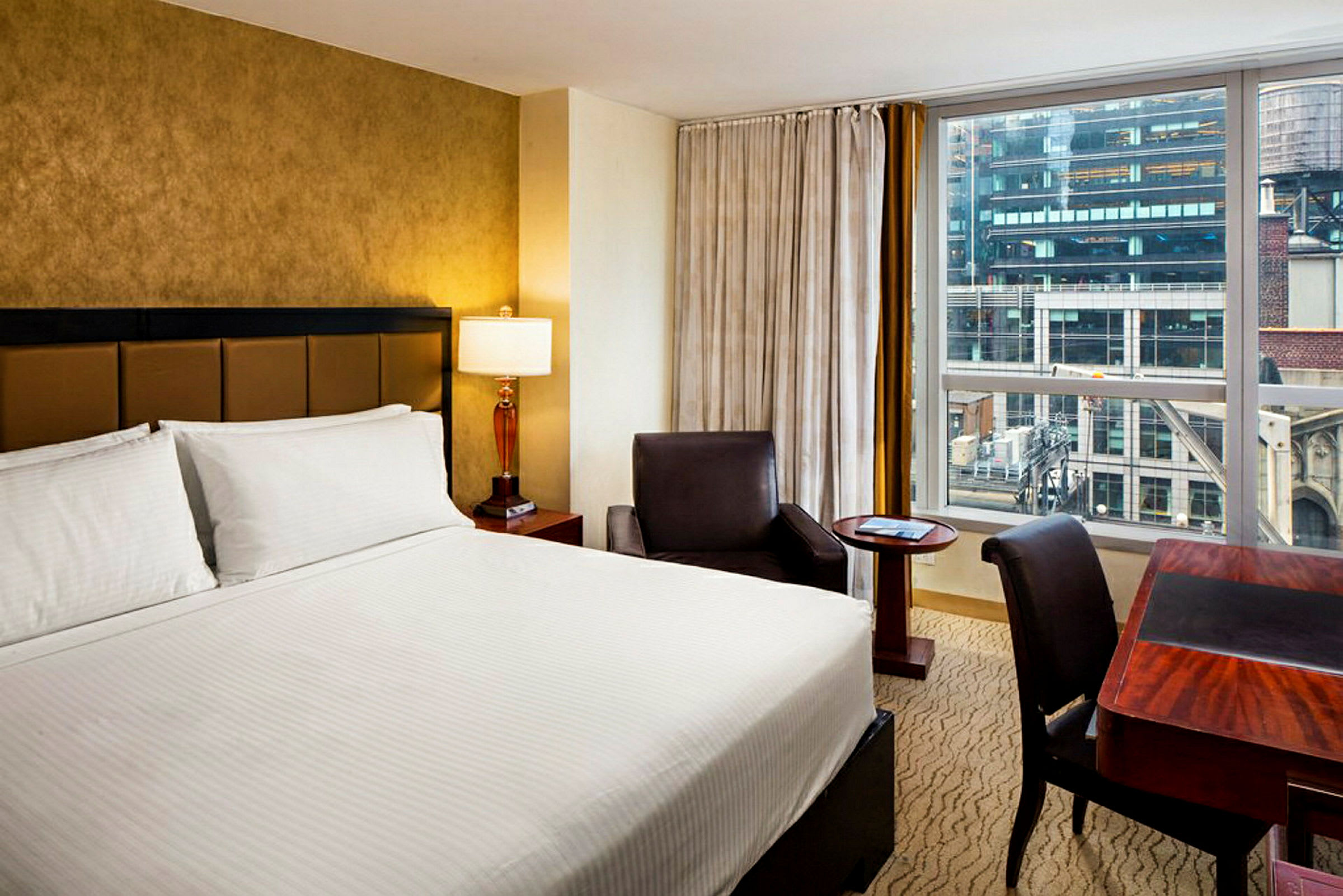 Hotellrum med dubbelsäng, skrivbord och fåtölj. (AI-genererad text)