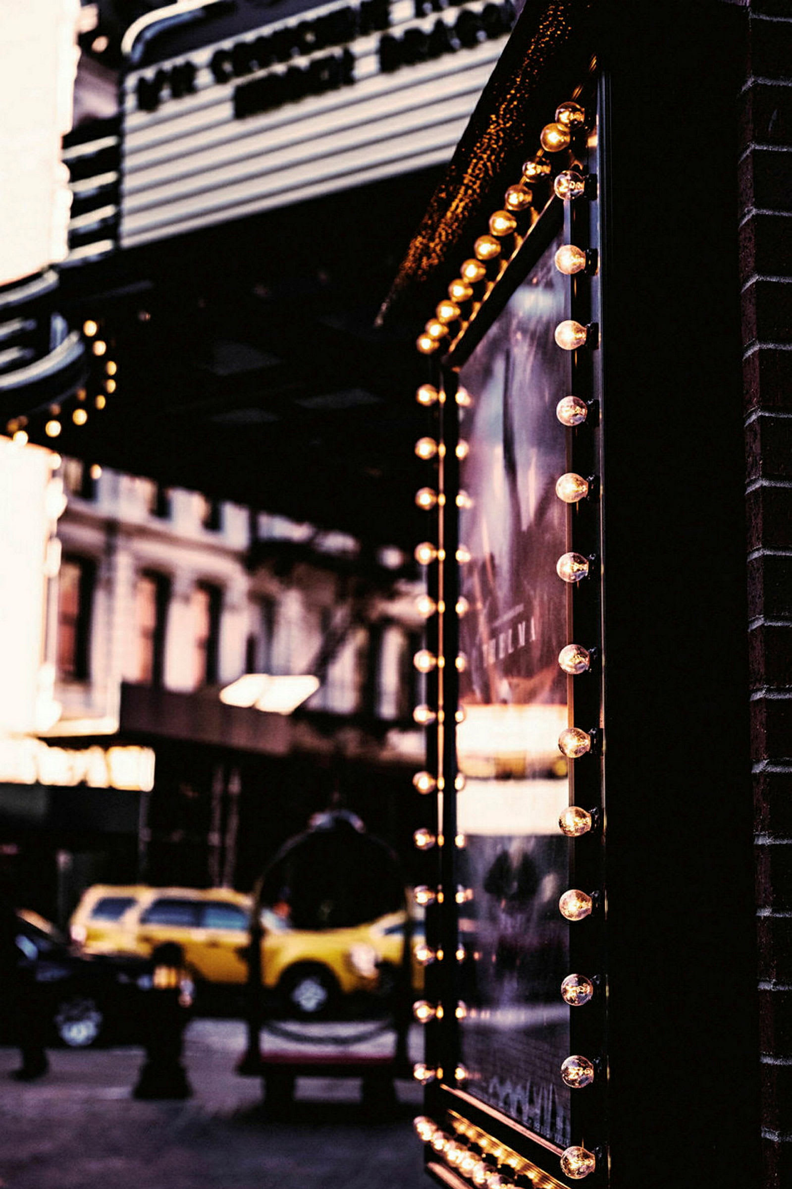 En skylt med små lampor runt kanten hänger utanför en byggnad. I bakgrunden syns gatubild med bilar och fasader. (AI-genererad text)