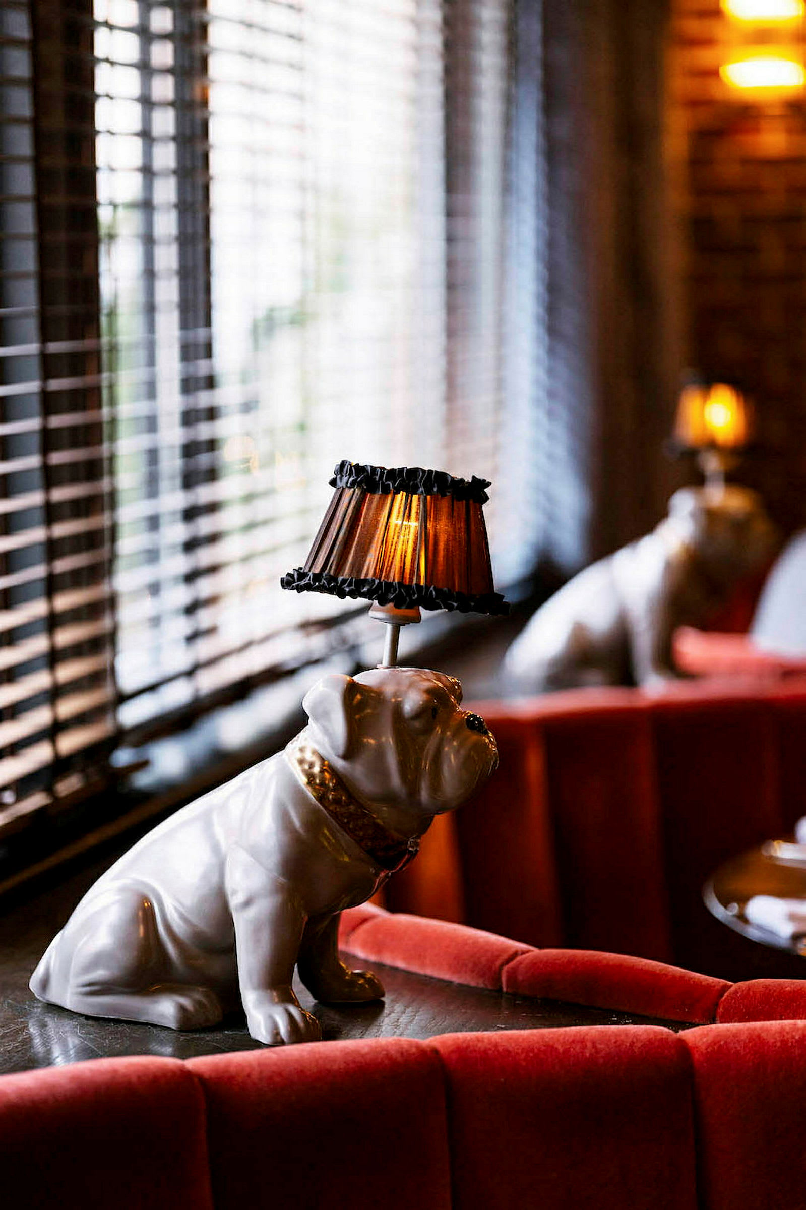 En dekorativ lampa formad som en bulldogstaty med en lampskärm på huvudet står på ett bord fyllt med röda soffor. (AI-genererad text)