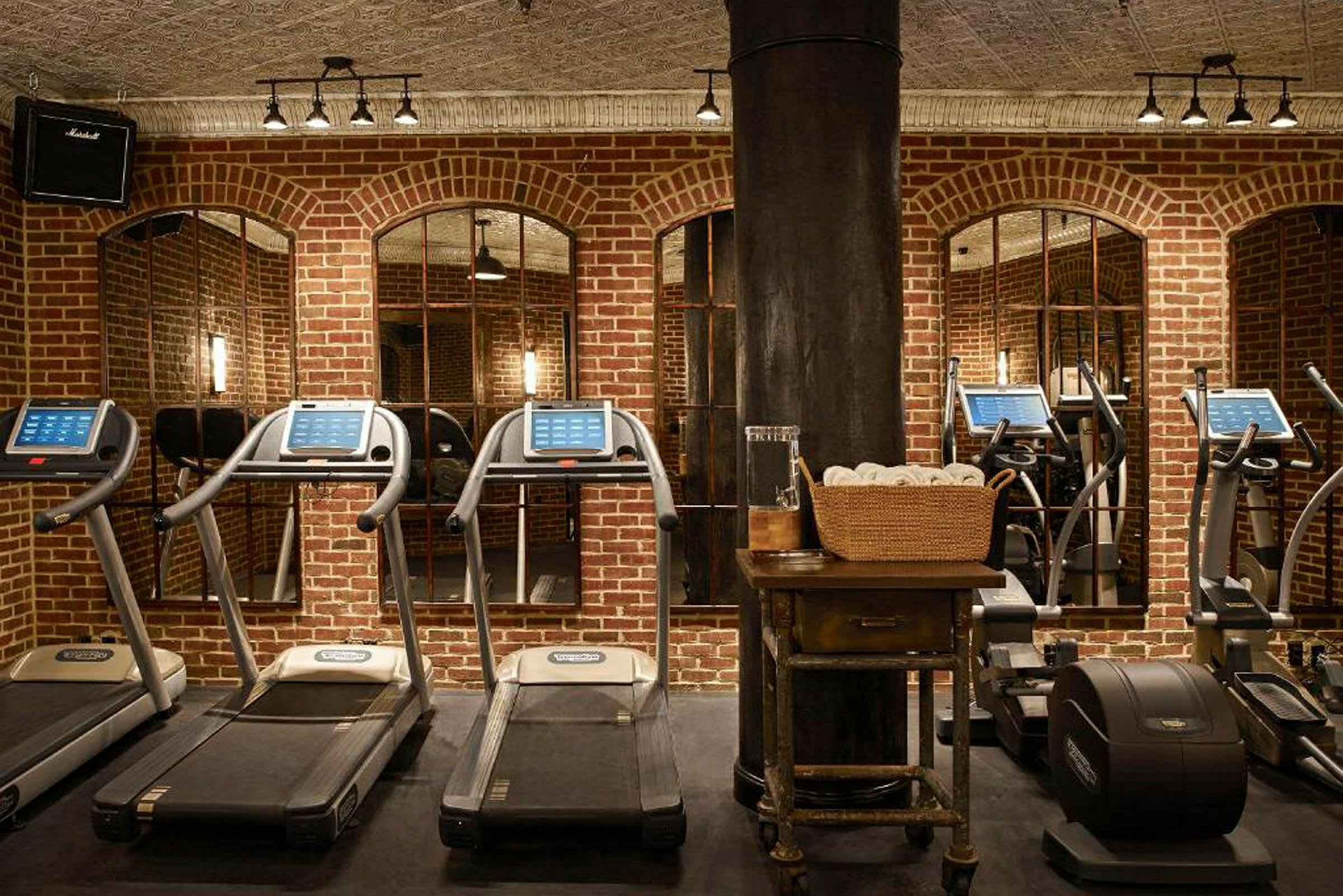 Ett gym med löpband och träningsutrustning framför en tegelvägg. (AI-genererad text)