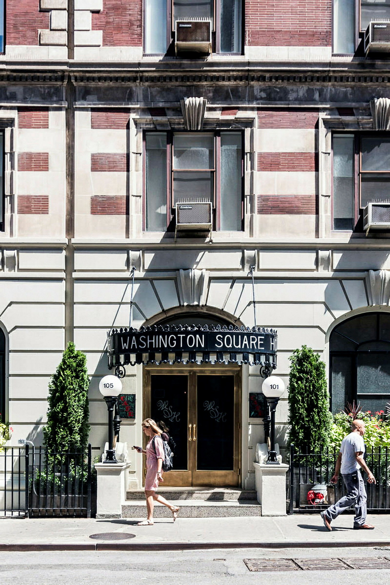 En byggnad med texten 'Washington Square Hotel' ovanför entrédörrarna och två personer som går på trottoaren framför. (AI-genererad text)