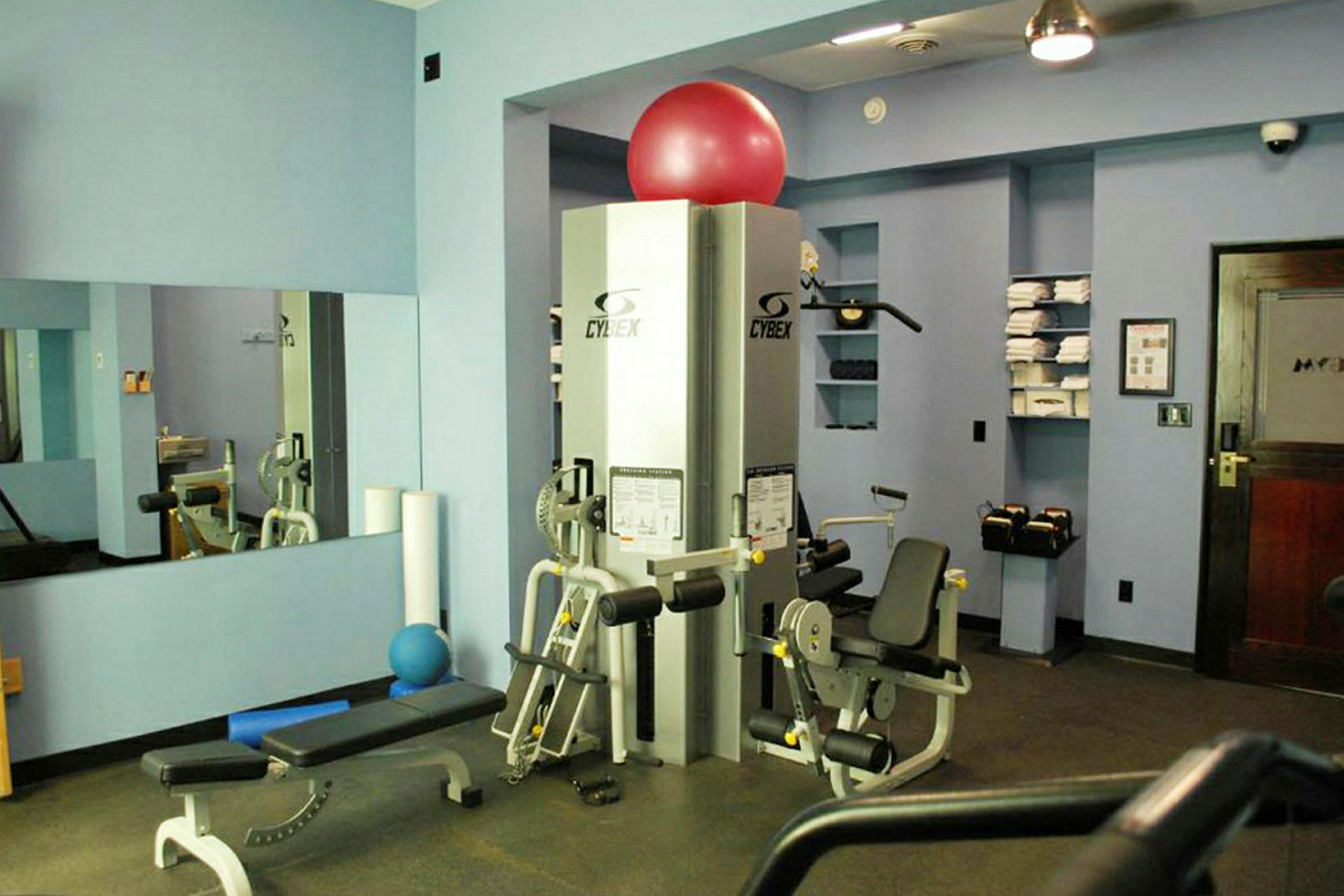 Ett gym med träningsutrustning och bänkar, blå väggar och en röd träningsboll. (AI-genererad text)