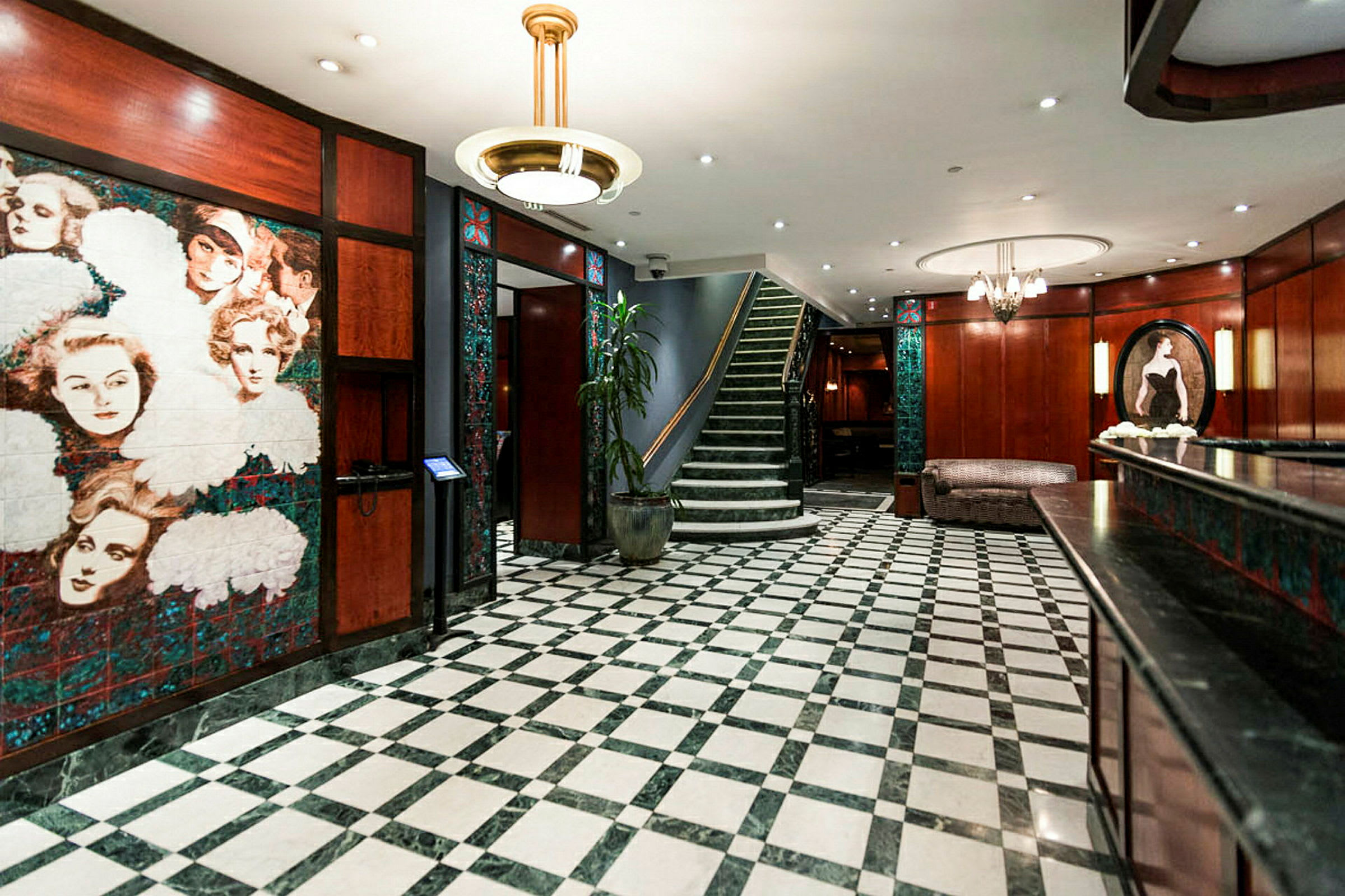 En hotellobby med rutigt golv, träpaneler och en trappa i bakgrunden. (AI-genererad text)