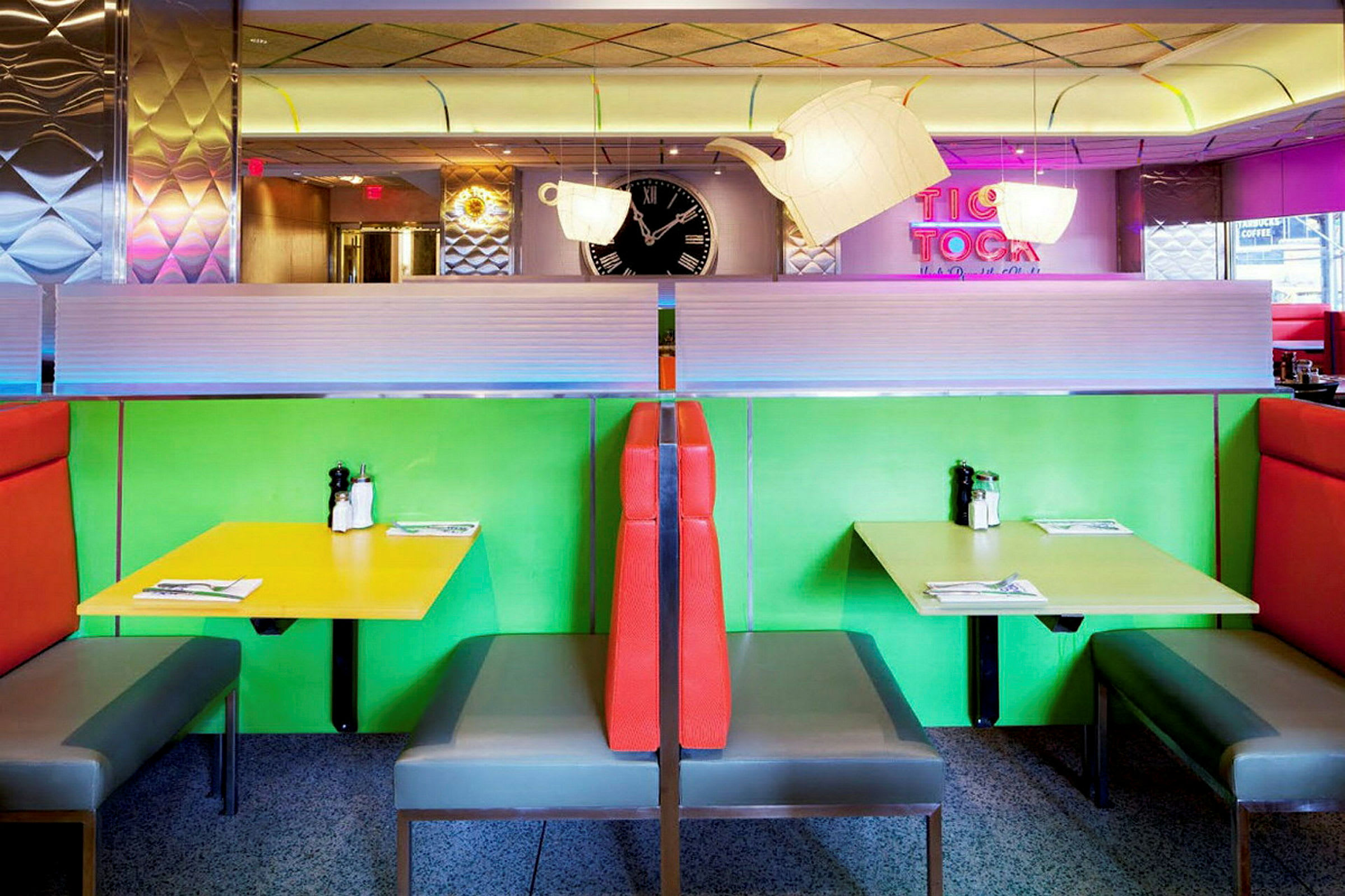 Färgglada sittbås i en retrorestaurang med grön och gul färgsättning på borden samt röd stoppning på ryggstöden. (AI-genererad text)
