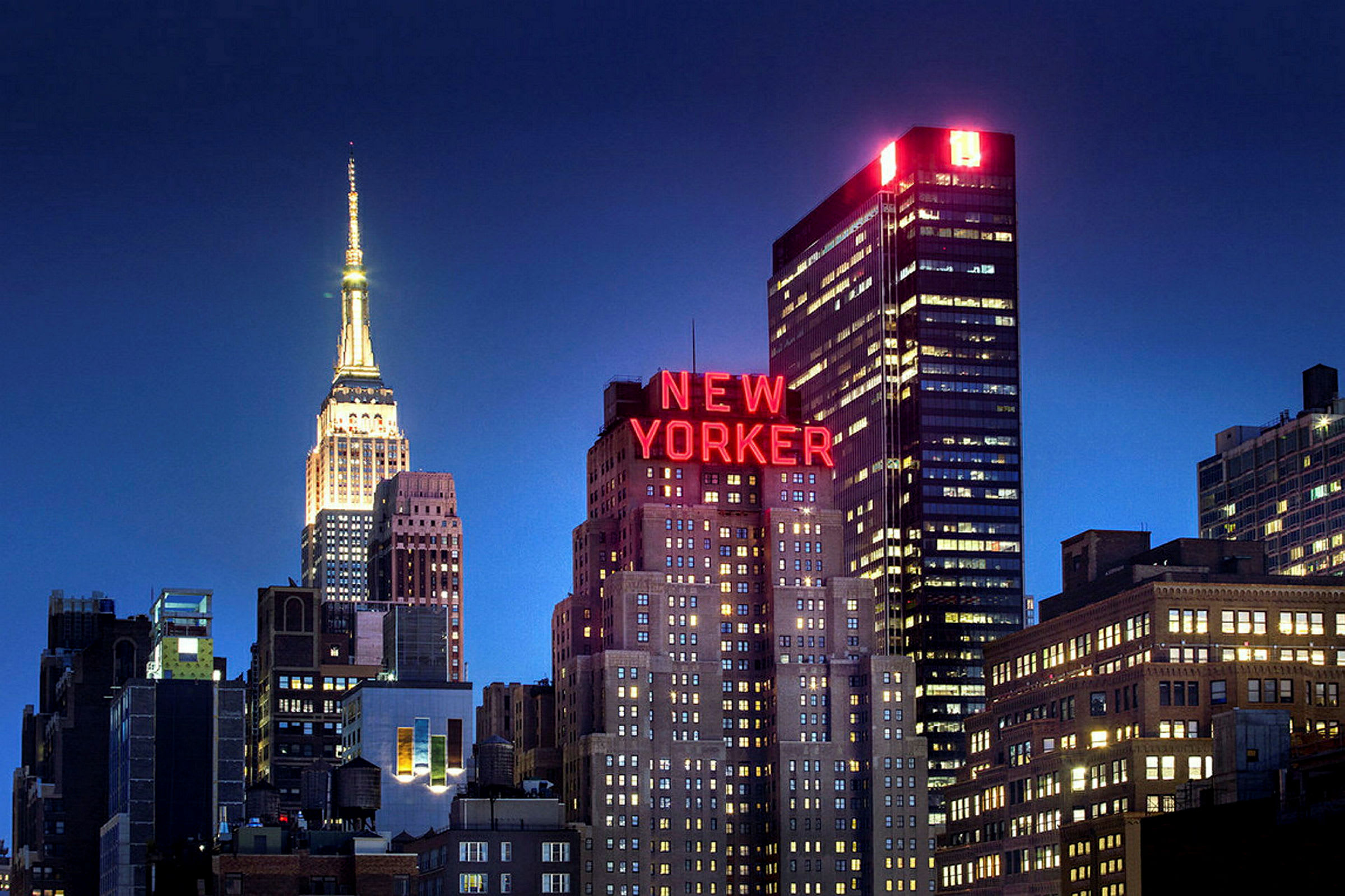 En stadssilhuett med upplysta byggnader och skylten "New Yorker" synlig mot en mörk natthimmel. (AI-genererad text)