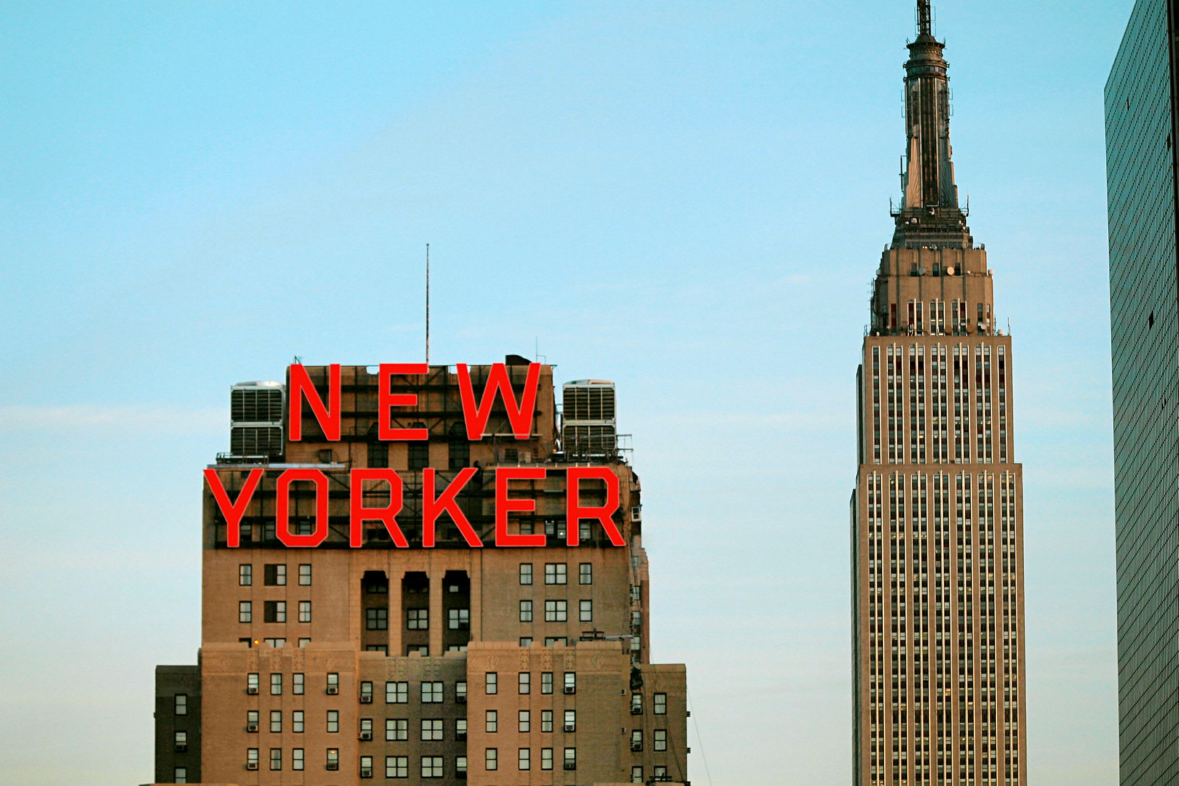 Bild av byggnaden med skylten "New Yorker" och Empire State Building i bakgrunden. (AI-genererad text)