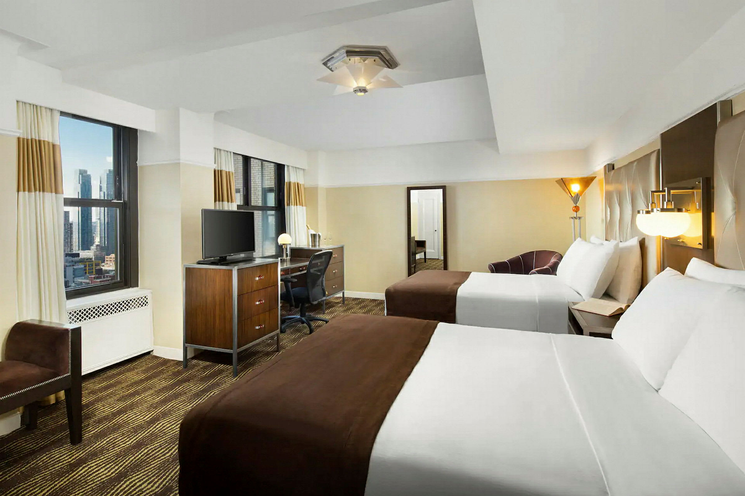 Ett hotellrum med två dubbelsängar, skrivbord, TV och två stora fönster. (AI-genererad text)