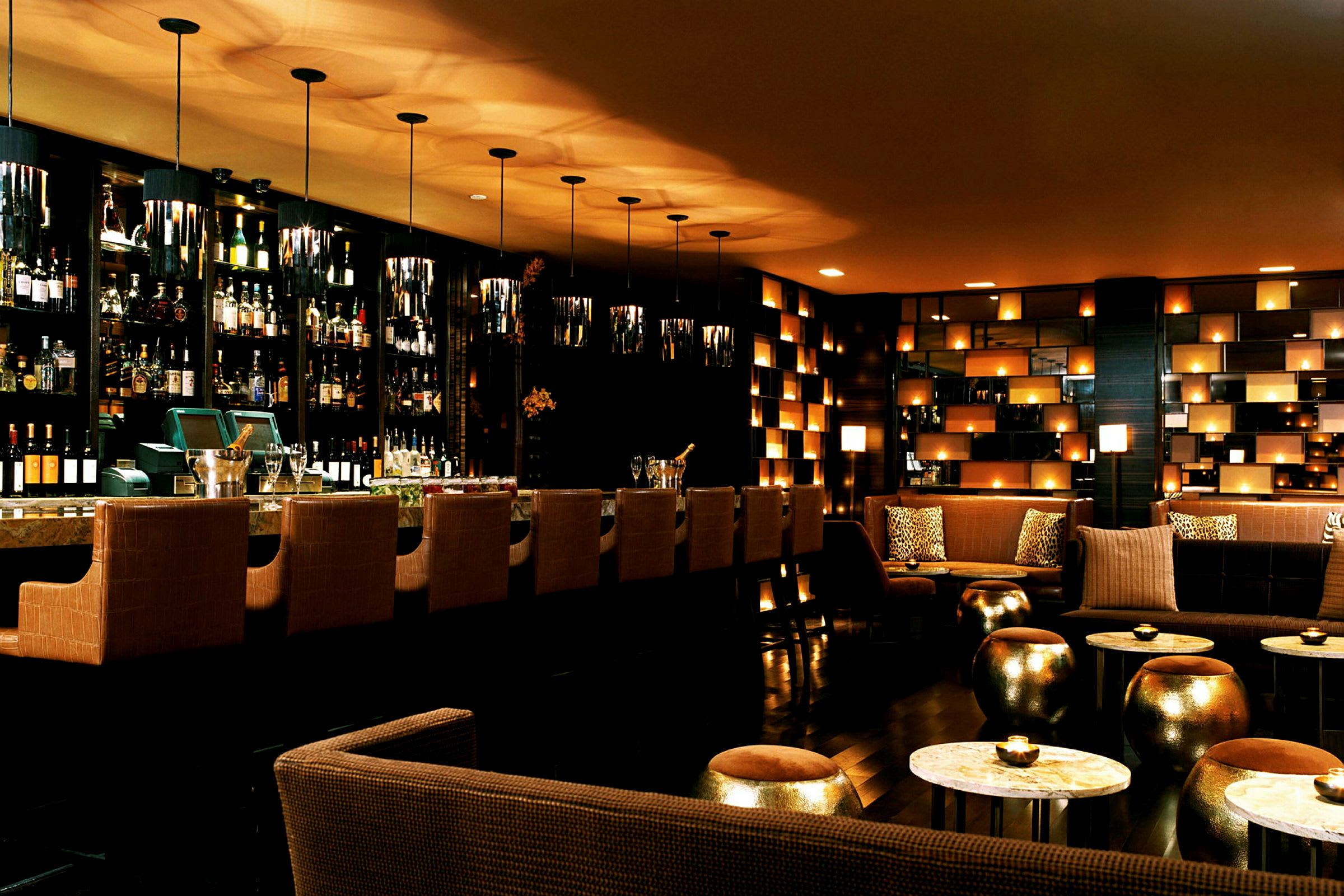 En elegant bar med hög ryggstolar vid bardisken, flaskor i bakgrunden, samt soffor och bord med mjuk belysning. (AI-genererad text)