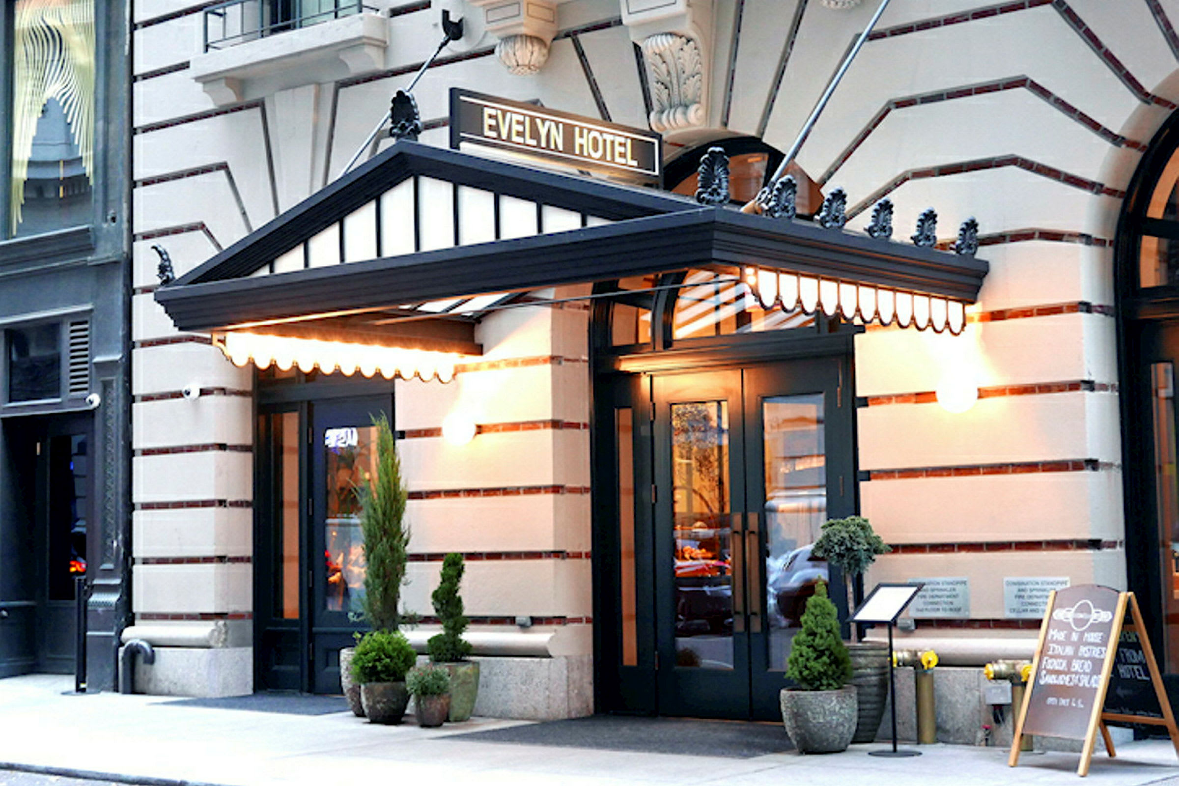 Hotellentré med en svart baldakin och texten "Evelyn Hotel" på en skylt ovanför. Utanför finns krukväxter och en meny på ett ställ. (AI-genererad text)