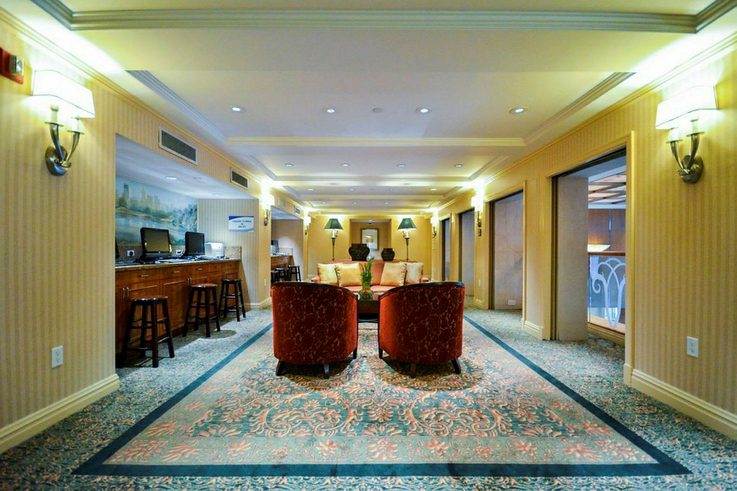 En elegant lounge med soffa och fåtöljer på en matta, omgiven av bord och datorskärmar. (AI-genererad text)