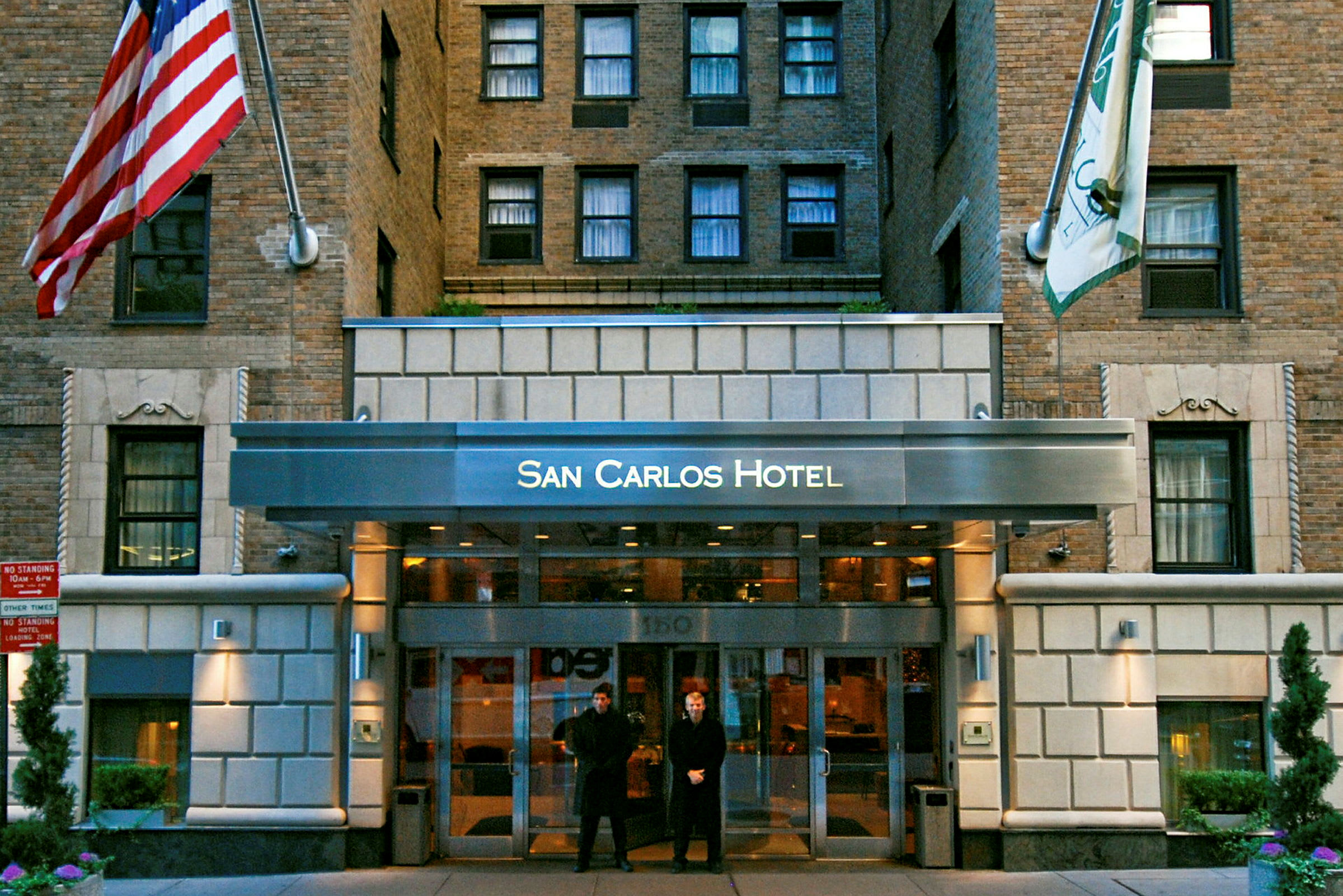 Entrén till San Carlos Hotel, ett byggnadsfasad med tegel och flaggor. (AI-genererad text)