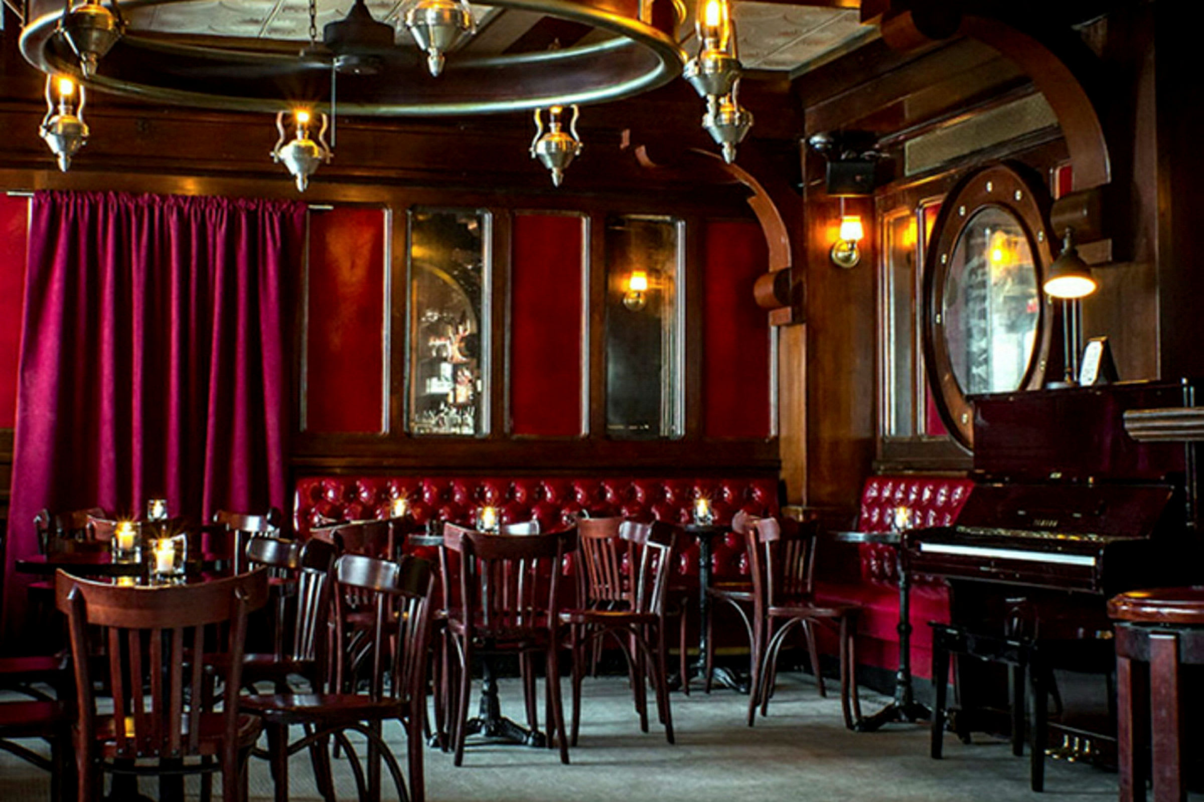 En interiör av en restaurang eller bar med träpaneler, röda sammetsgardiner och ett piano. (AI-genererad text)