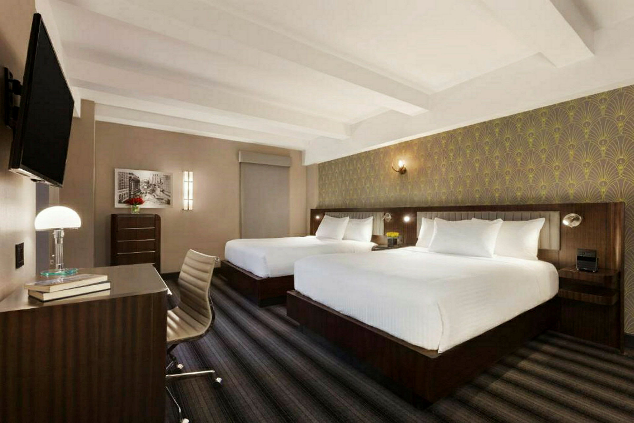 Ett hotellrum med två stora sängar, en arbetsplats och en väggmonterad TV. (AI-genererad text)