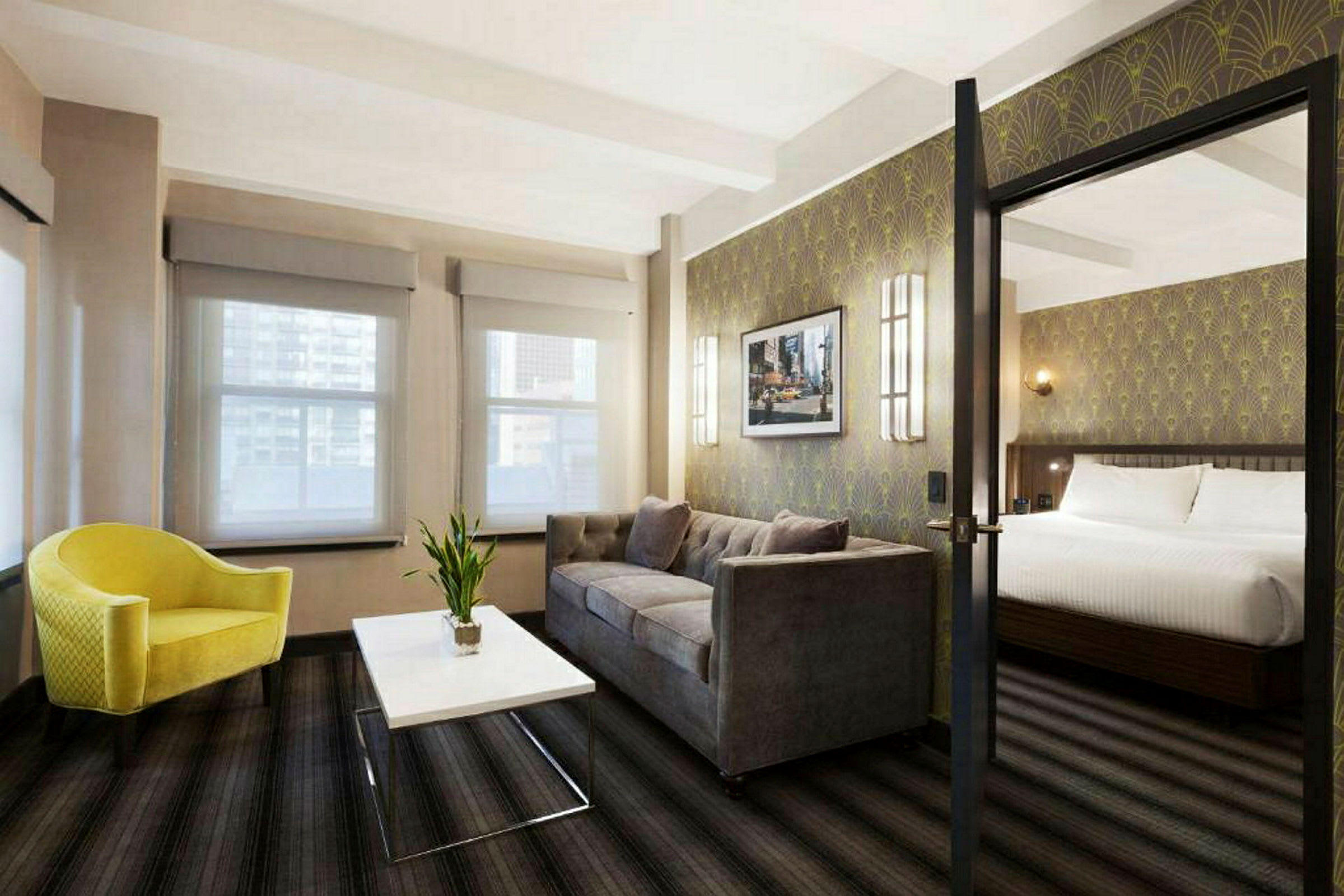 Ett hotellrum med en sittgrupp bestående av en gul fåtölj, ett vitt soffbord och en grå soffa. I bakgrunden syns en sovplats med en dubbelsäng. (AI-genererad text)