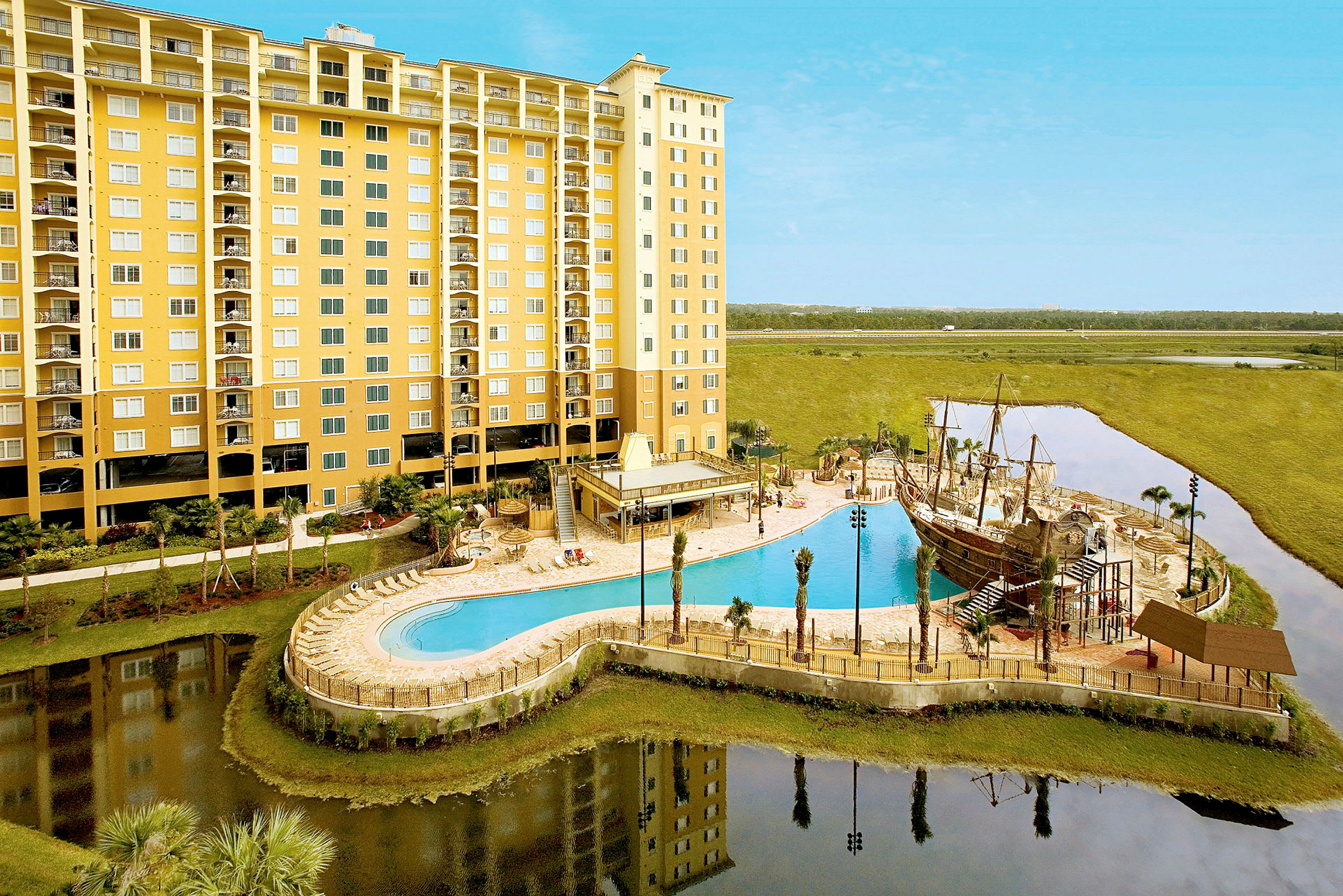 Ett större hotell med gul fasad, i förgrunden syns en pool och ett område med en lekplats som har en pirattemapark. (AI-genererad text)