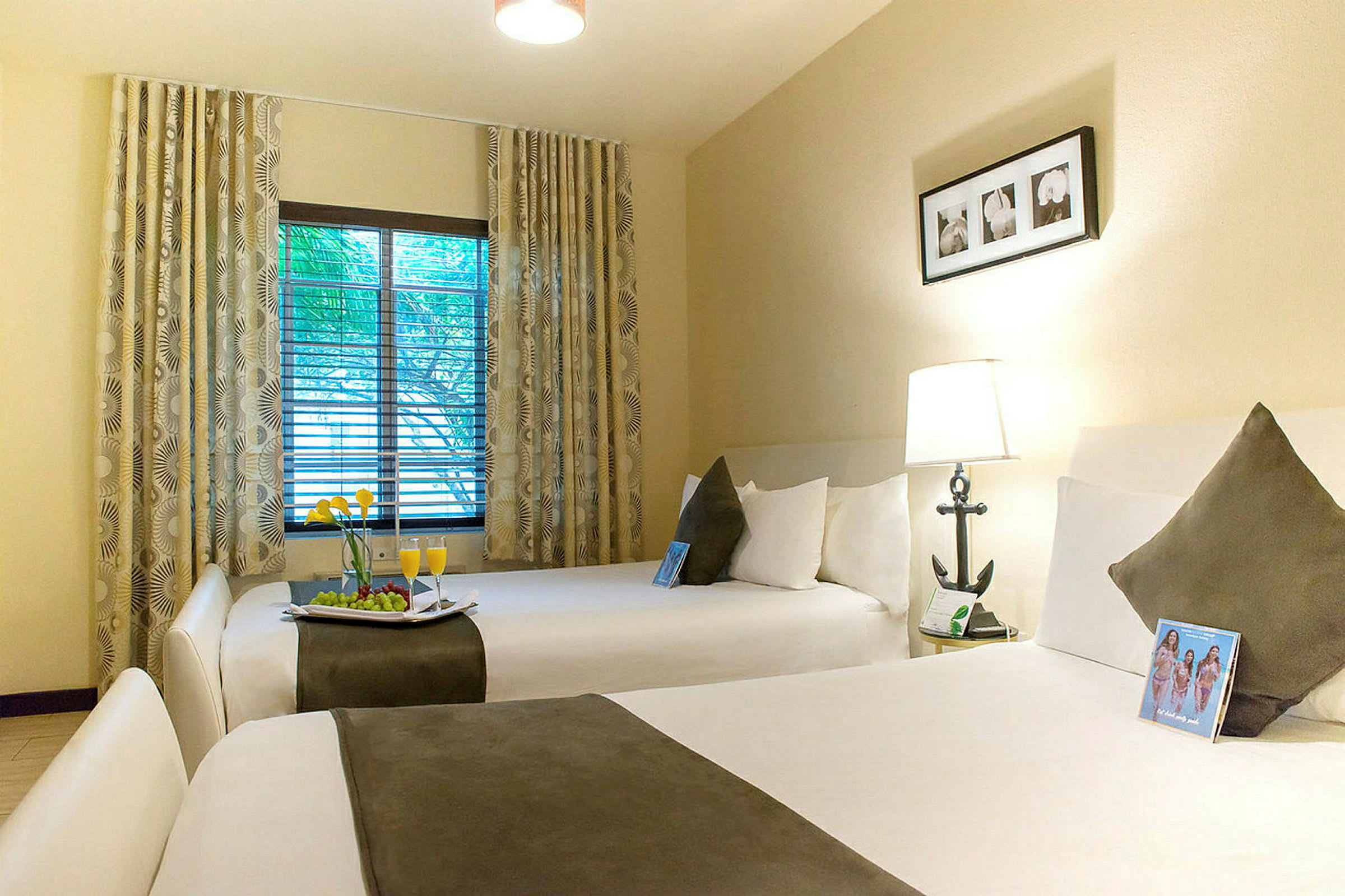 Ett hotellrum med två breda sängar, varsin kudde och pläd. Ett fönster med draperier och utsikt över träd. (AI-genererad text)