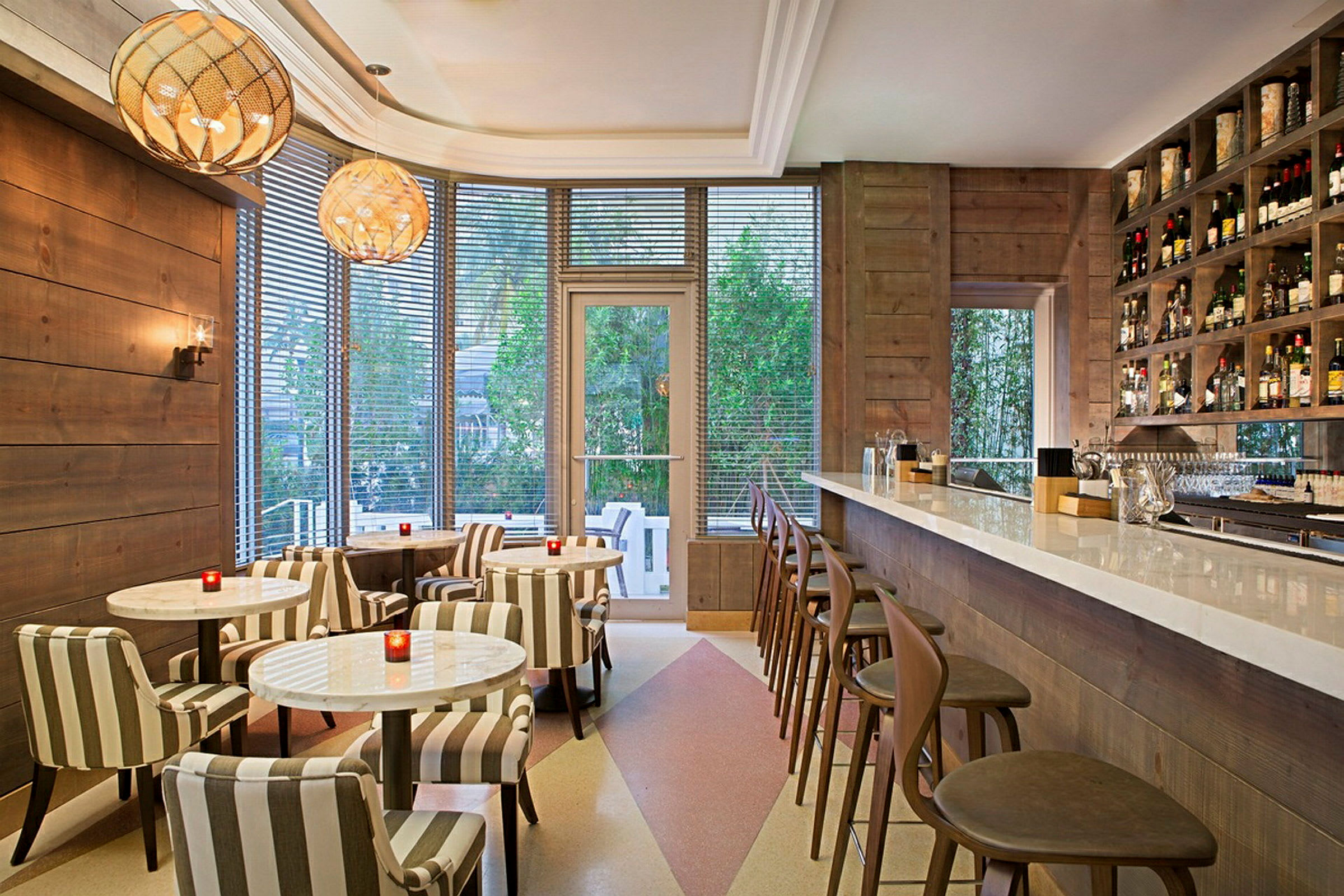 En snyggt inredd café- eller barinteriör med ljusa möbler, en lång bardisk till höger och bord med stolar till vänster. (AI-genererad text)