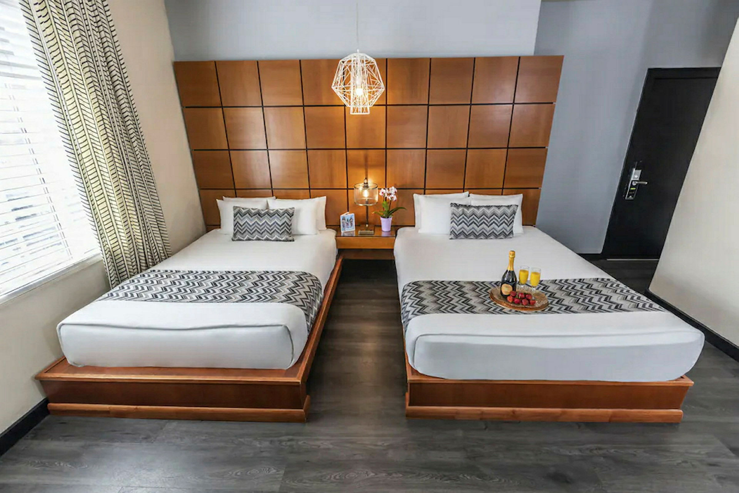 Bild av ett hotellrum med två enkelsängar med vita sängkläder och mönstrade överkast. Rummet har en träpanel på väggen och ett nattduksbord med en blomma mellan sängarna. (AI-genererad text)