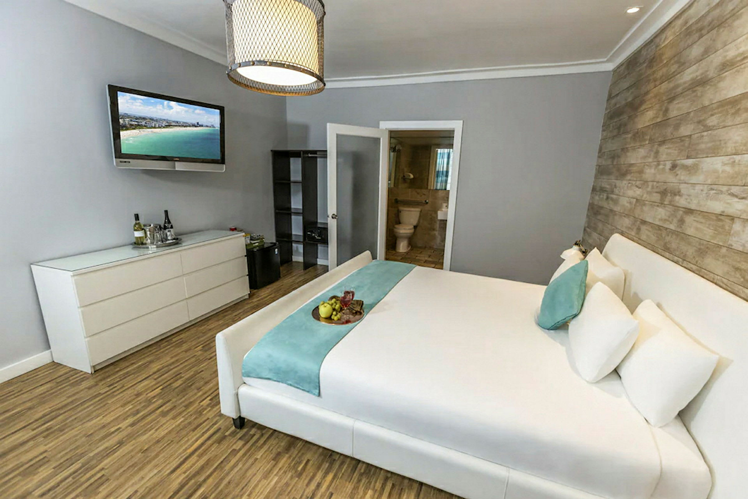 Ett hotellrum med en bred säng, en byrå med en TV ovanför och en öppning mot ett badrum. (AI-genererad text)