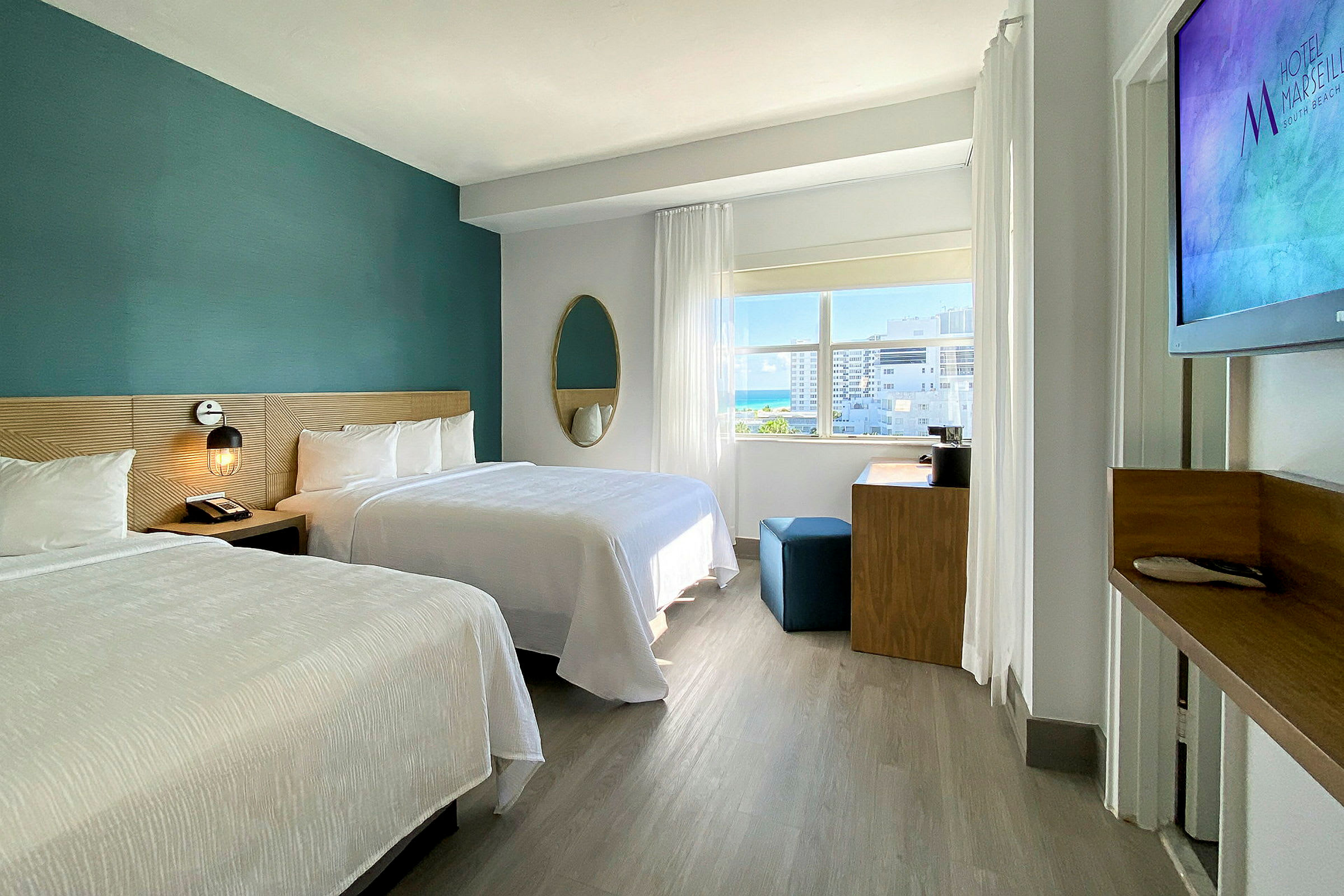 Ett modernt hotellrum med två dubbelsängar, ett skrivbord och ett stort fönster som släpper in naturligt ljus. (AI-genererad text)