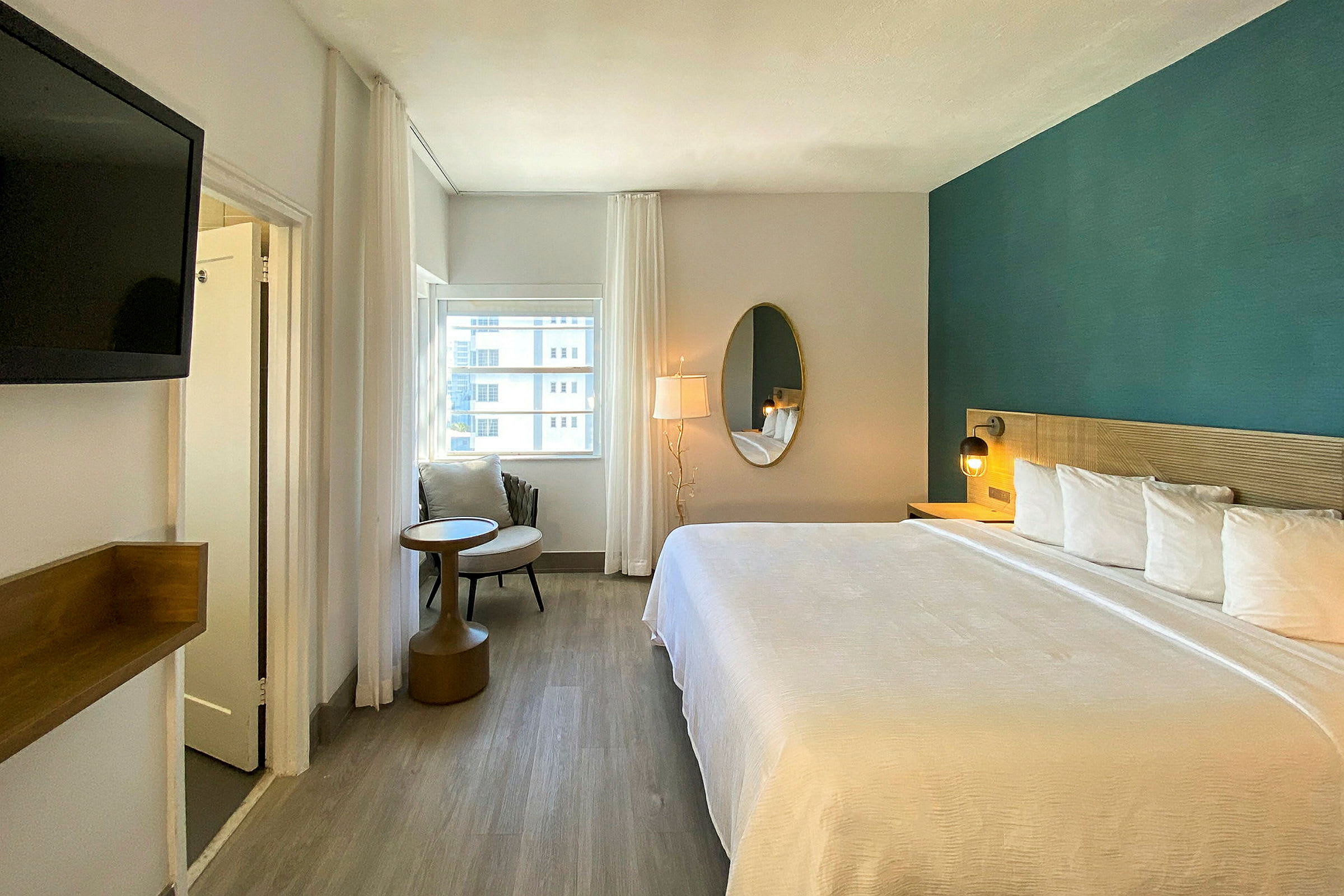 Modernt inrett hotellrum med stor säng, spegel, fåtölj och en fönstervy. (AI-genererad text)