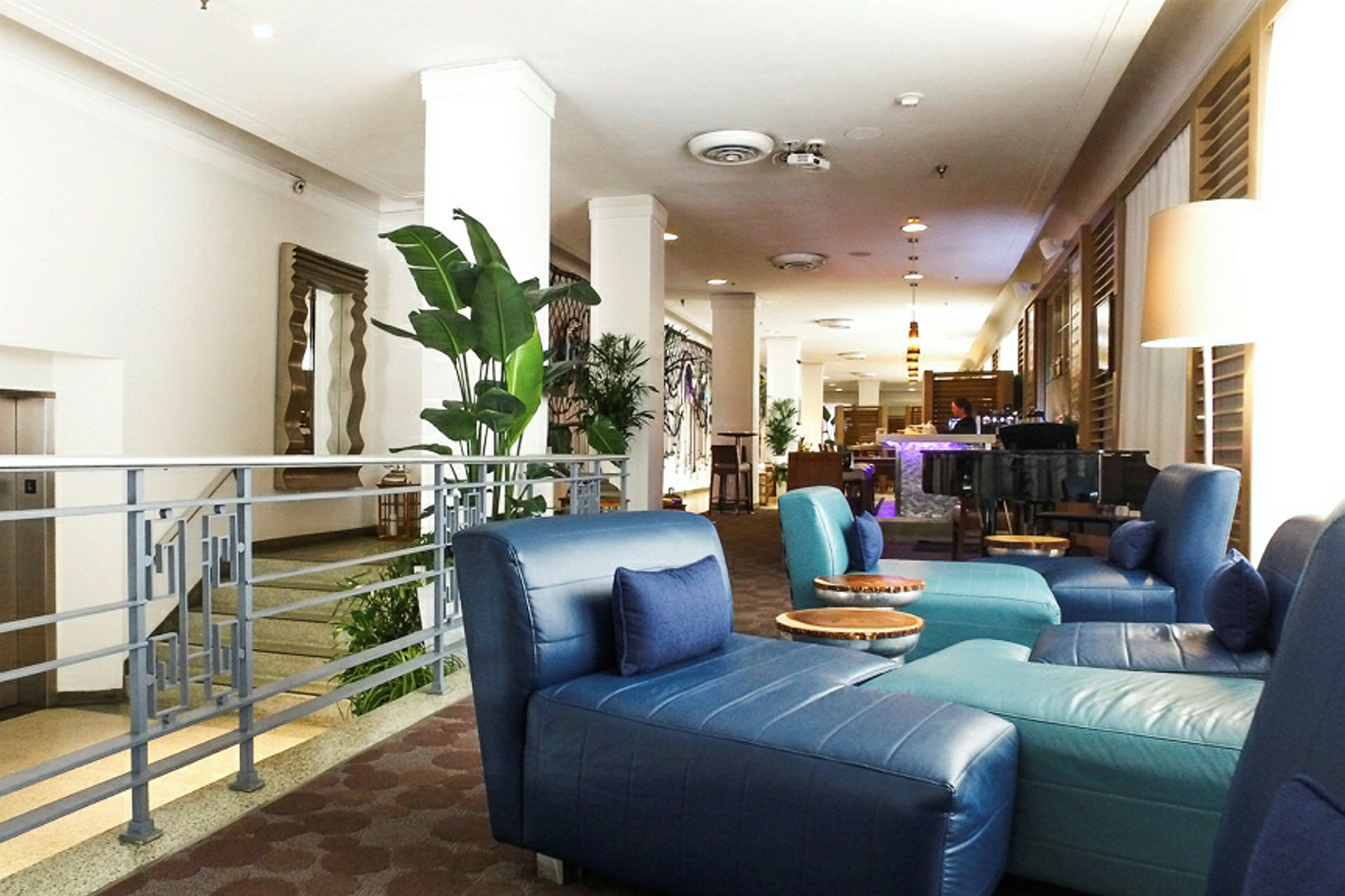 Bild av en hotellobby med blå sittstolar, gröna växter och en bar i bakgrunden. (AI-genererad text)