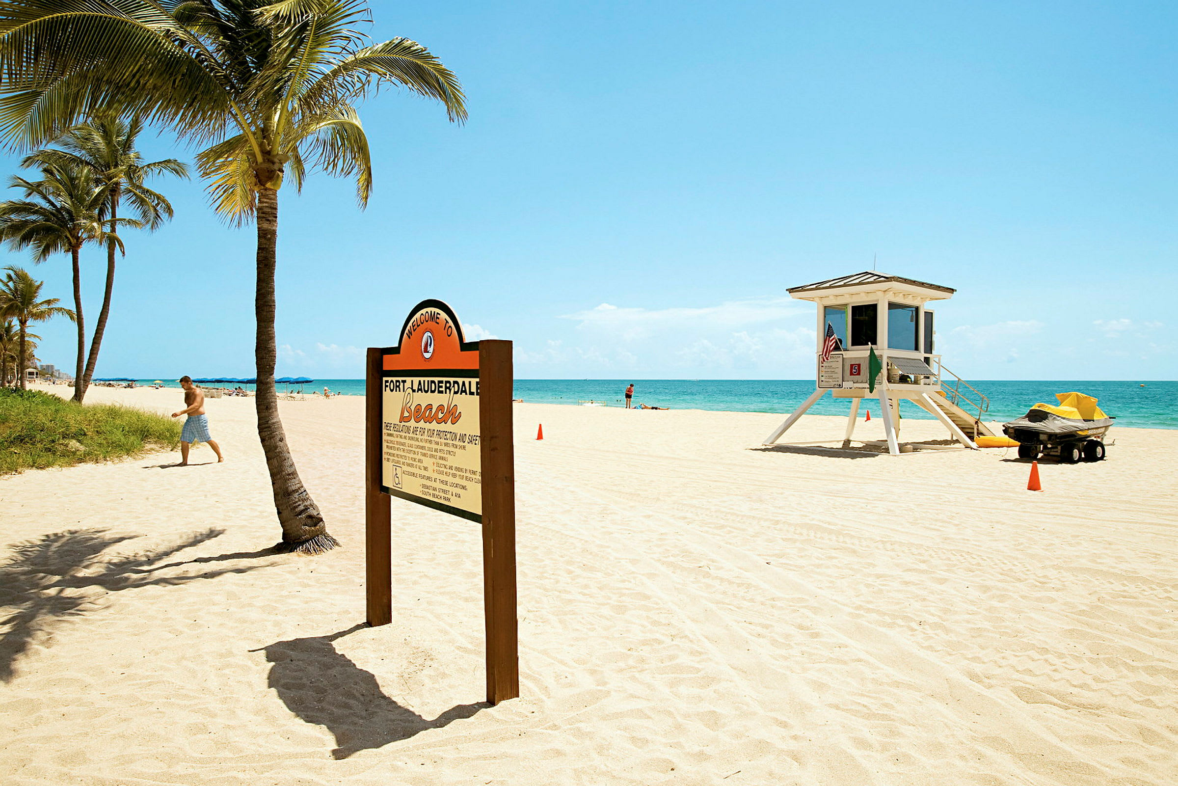 En sandstrand med palmer, en skylt som välkomnar till Fort Lauderdale Beach och ett livräddartorn. (AI-genererad text)
