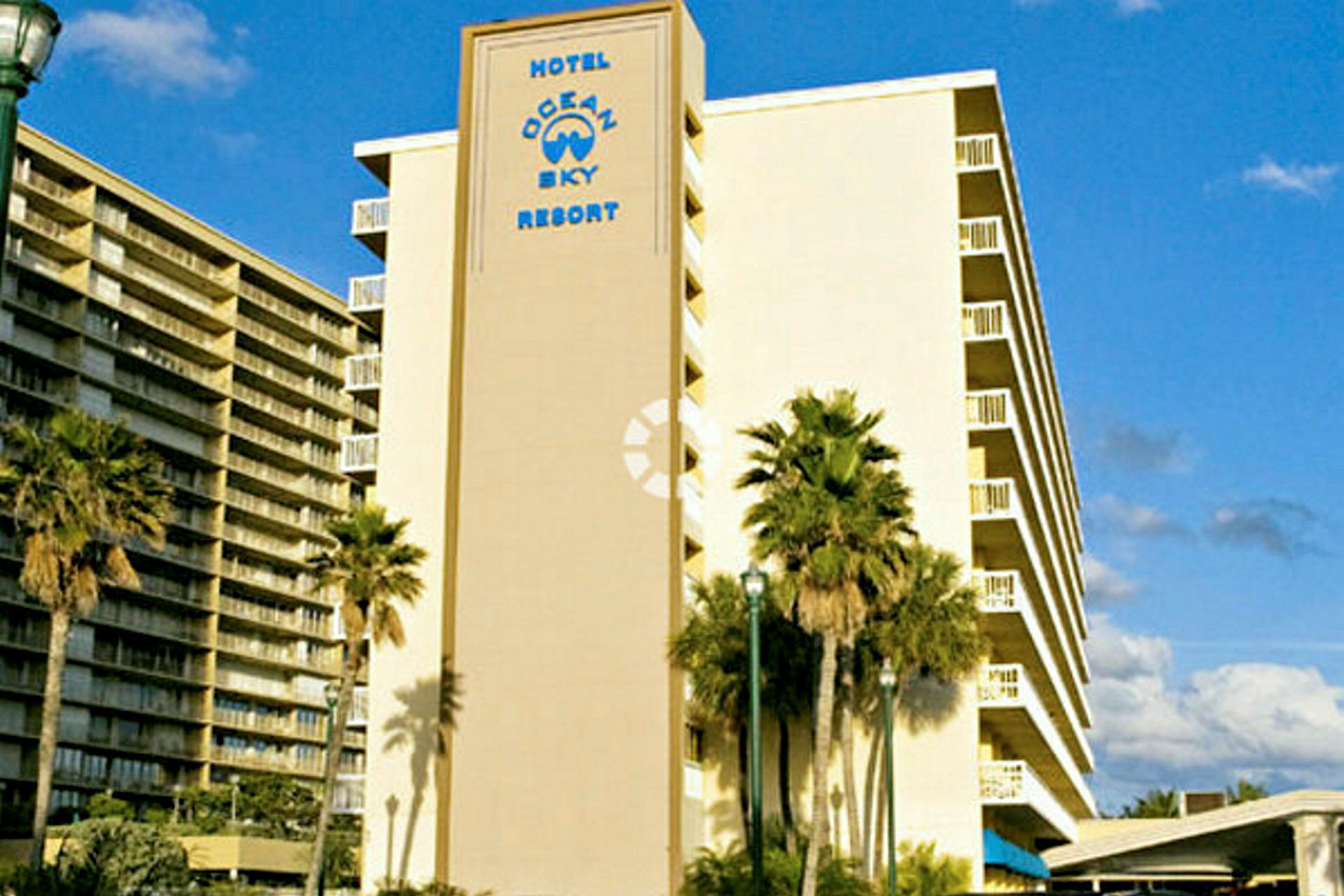 En bild av ett hotell med texten "Hotel Ocean Sky Resort" på fasaden. Palmer syns framför byggnaden. (AI-genererad text)