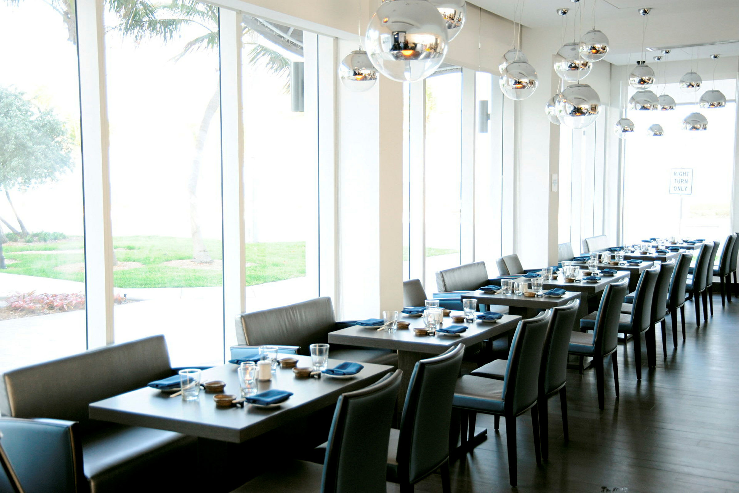 En modern restaurang med flera dukade bord, utsikt över grönska och stora fönster. (AI-genererad text)