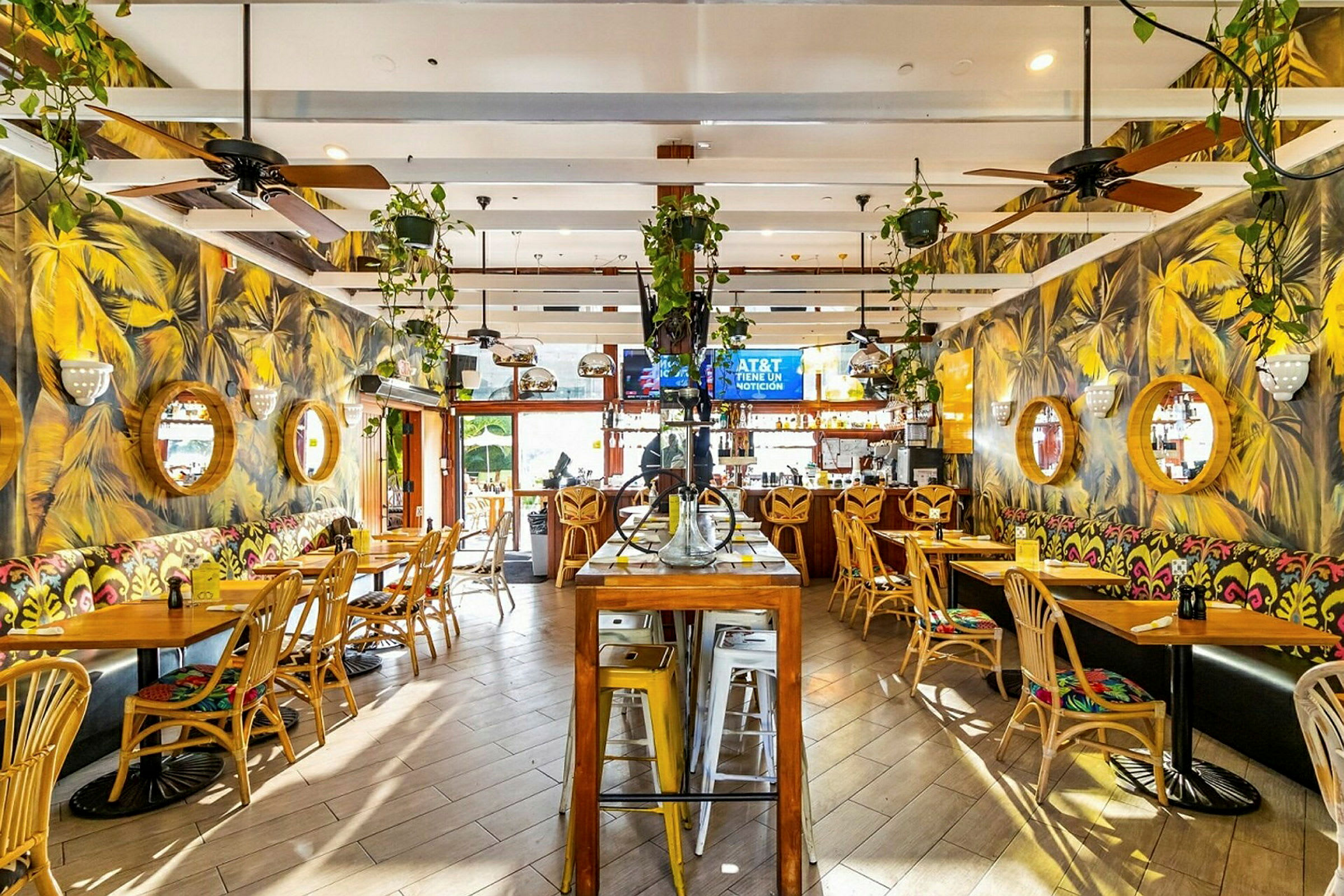 Inomhusmiljön i en restaurang med trästolar, bord och färgstarka väggmålningar. Väggarna pryds med runda speglar och växter hänger från taket. (AI-genererad text)