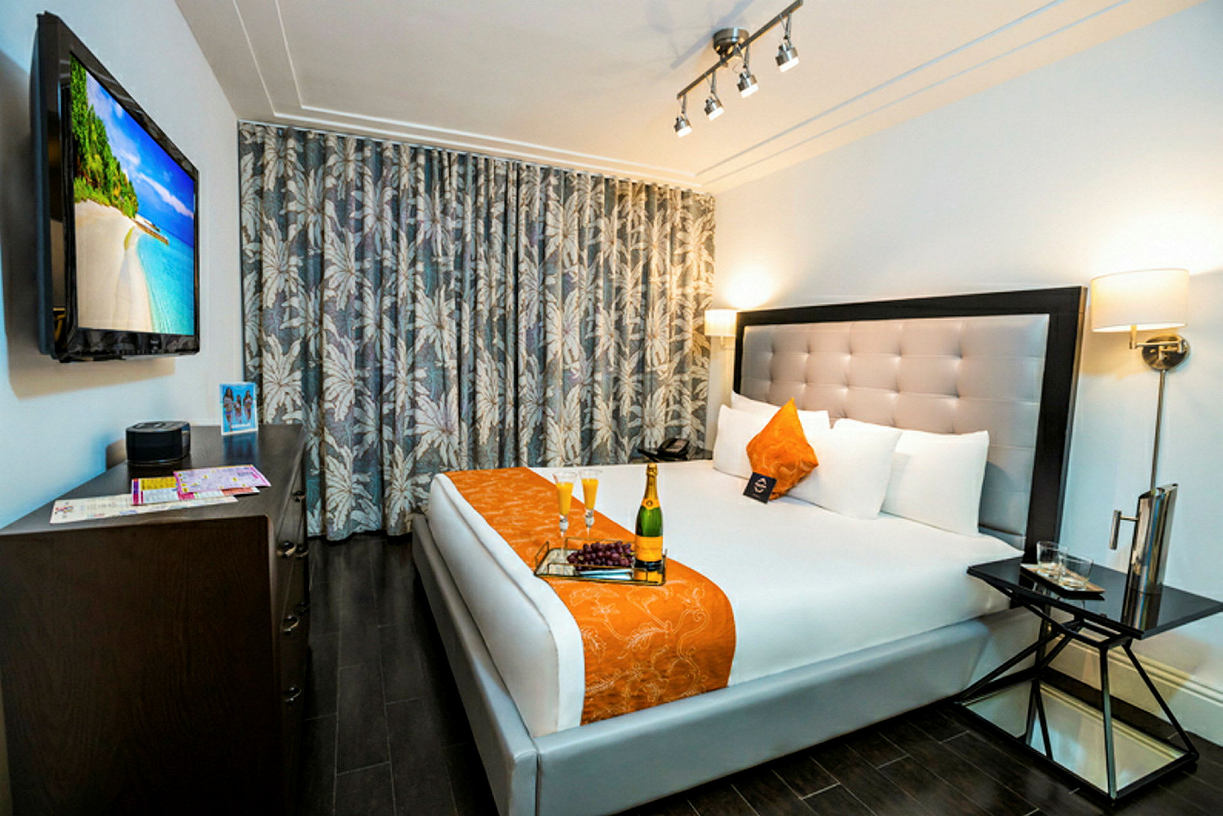 Ett hotellrum med en dubbelsäng klädd i vitt och orange, ett bord intill, och en TV på väggen. (AI-genererad text)