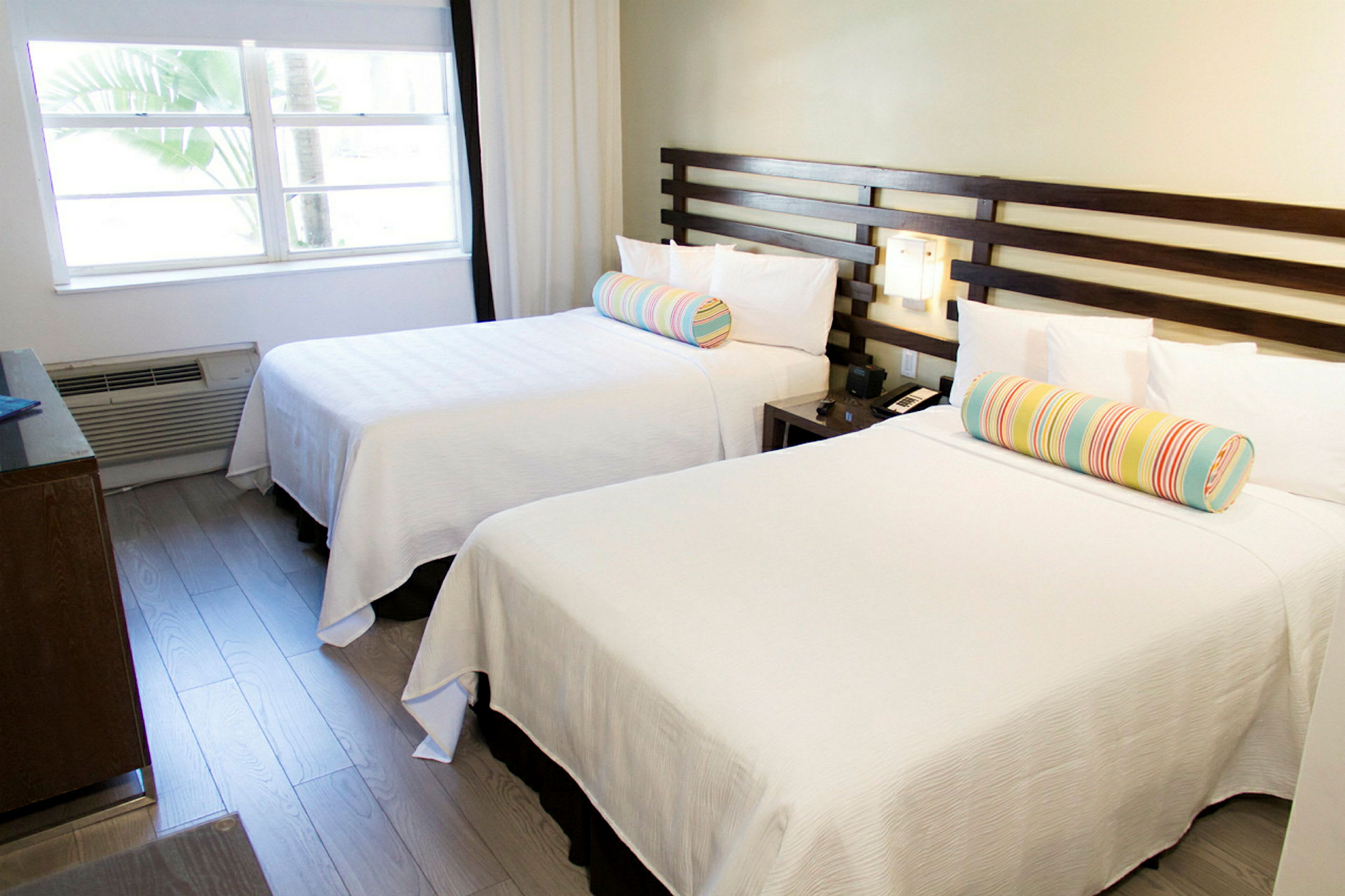 Ett hotellrum med två vita sängar och färgglada kuddar. (AI-genererad text)