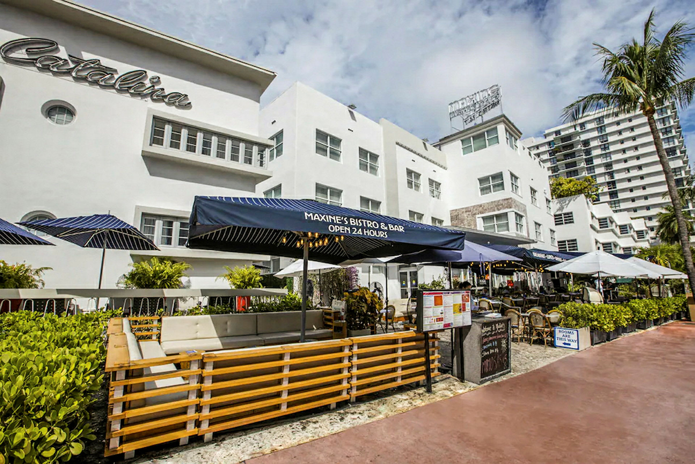En utomhusrestaurang med blå markiser framför en vit byggnad med namnet Catalina synligt. (AI-genererad text)