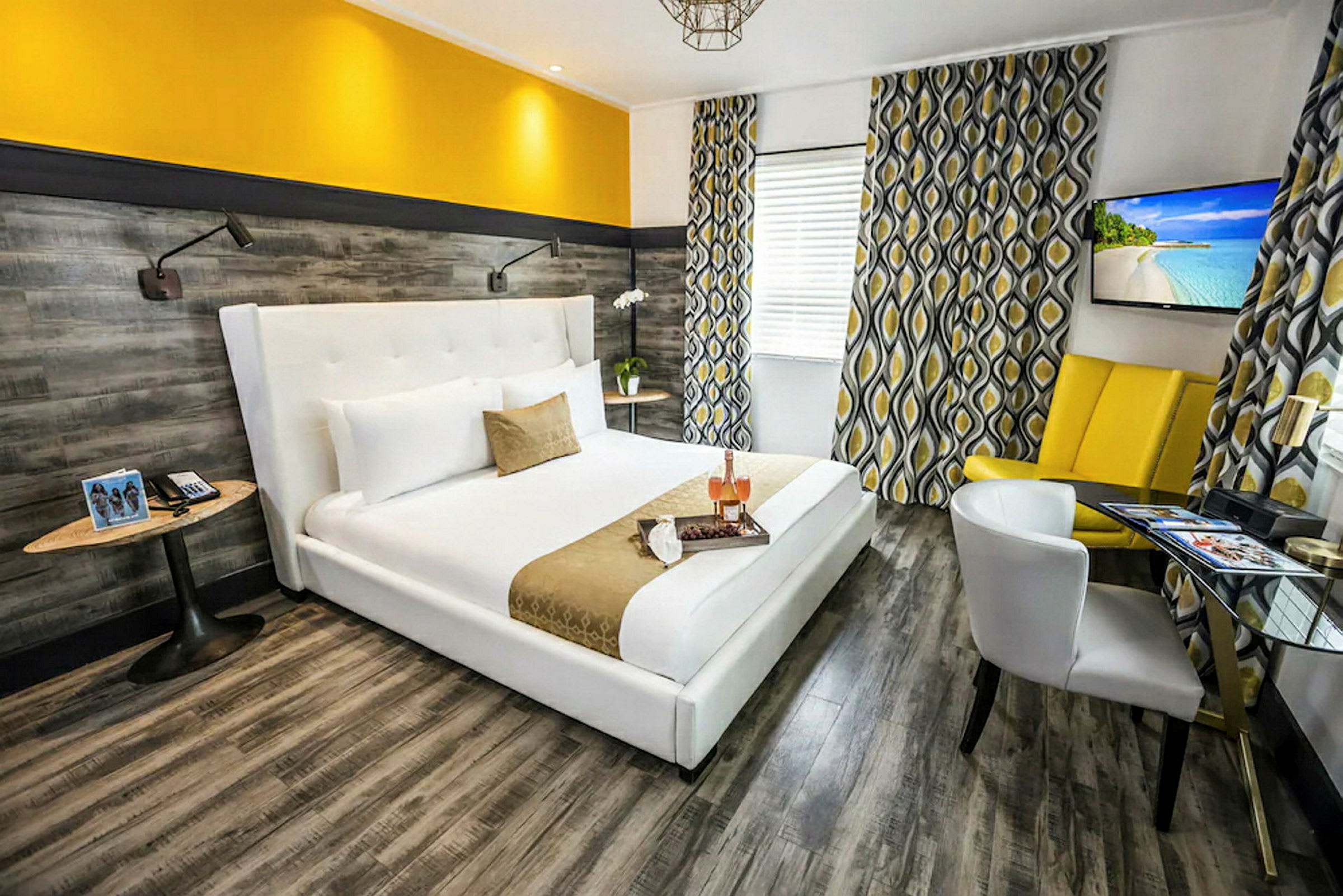 Ett modernt hotellrum med en bred, vit säng och gul accentdekor. Väggarna har ett träliknande mönster, och fönstren är dekorerade med mönstrade gardiner. (AI-genererad text)