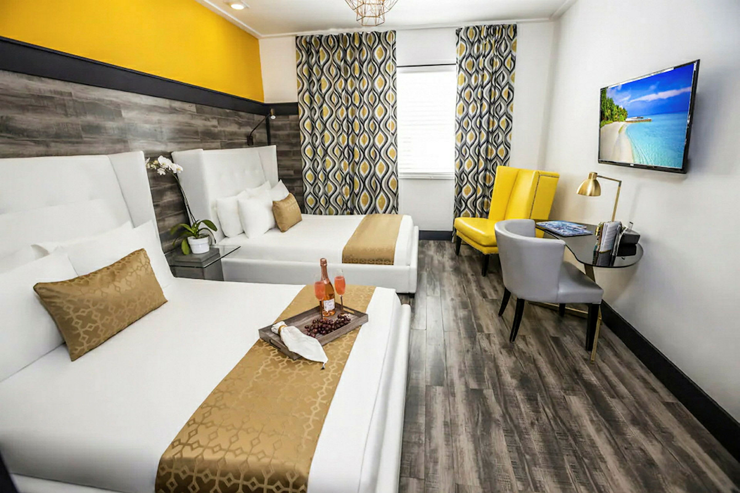 Ett hotellrum med två vita sängar, gul och grå inredning samt en TV på väggen. (AI-genererad text)