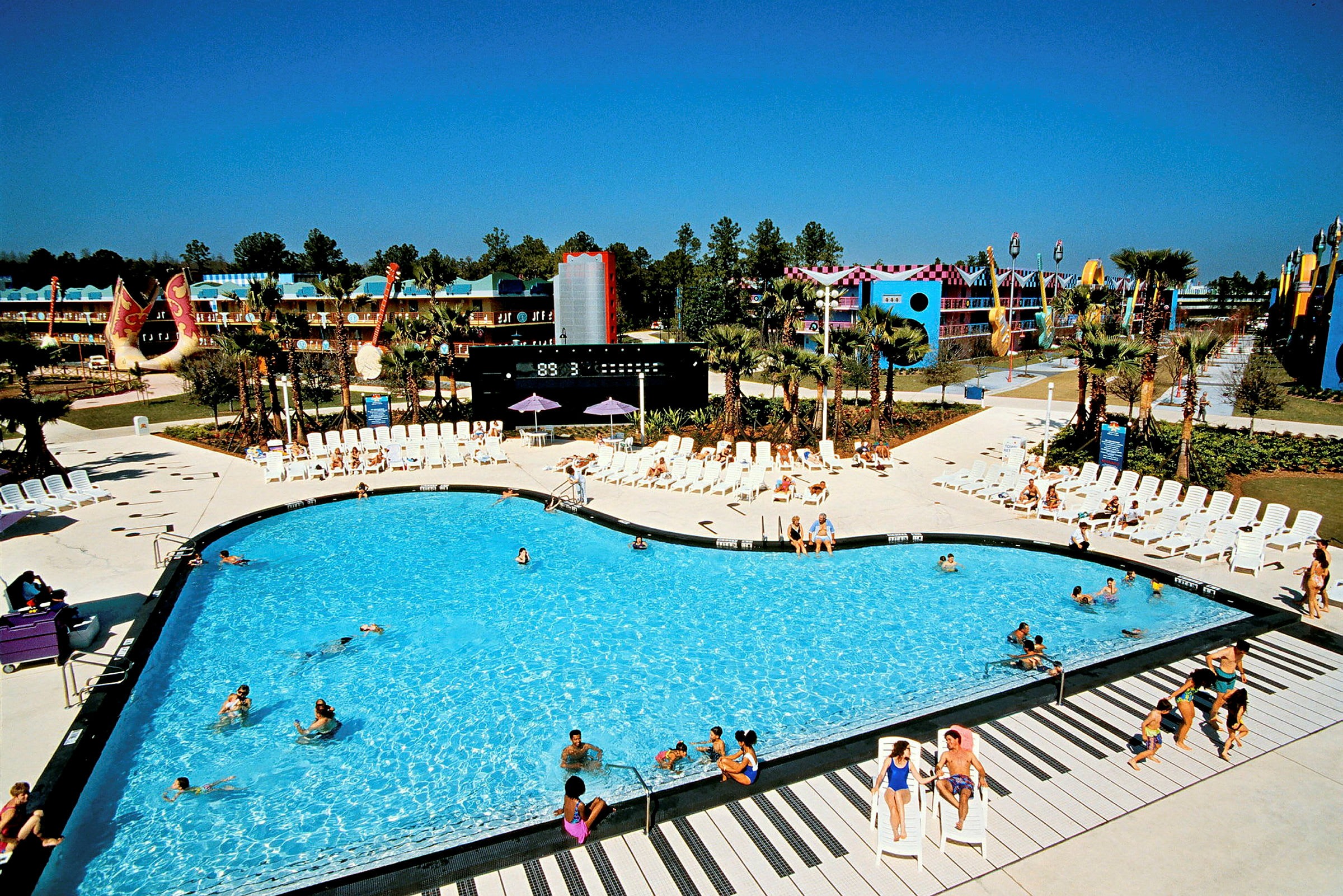 En simbassäng omgiven av solstolar vid ett semesterresort. Bakgrunden visar byggnader och dekorationer. (AI-genererad text)