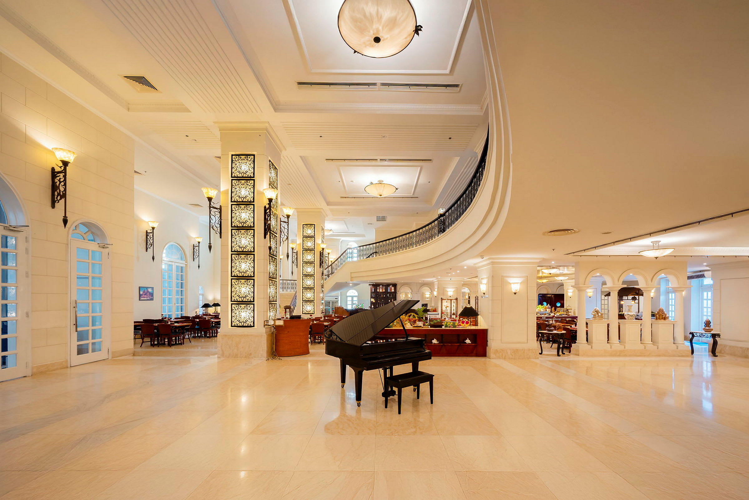 Ett elegant hotellatrium med stora fönster, valv och ljusa marmorgolv. En svart flygel står på golvet i mitten. (AI-genererad text)