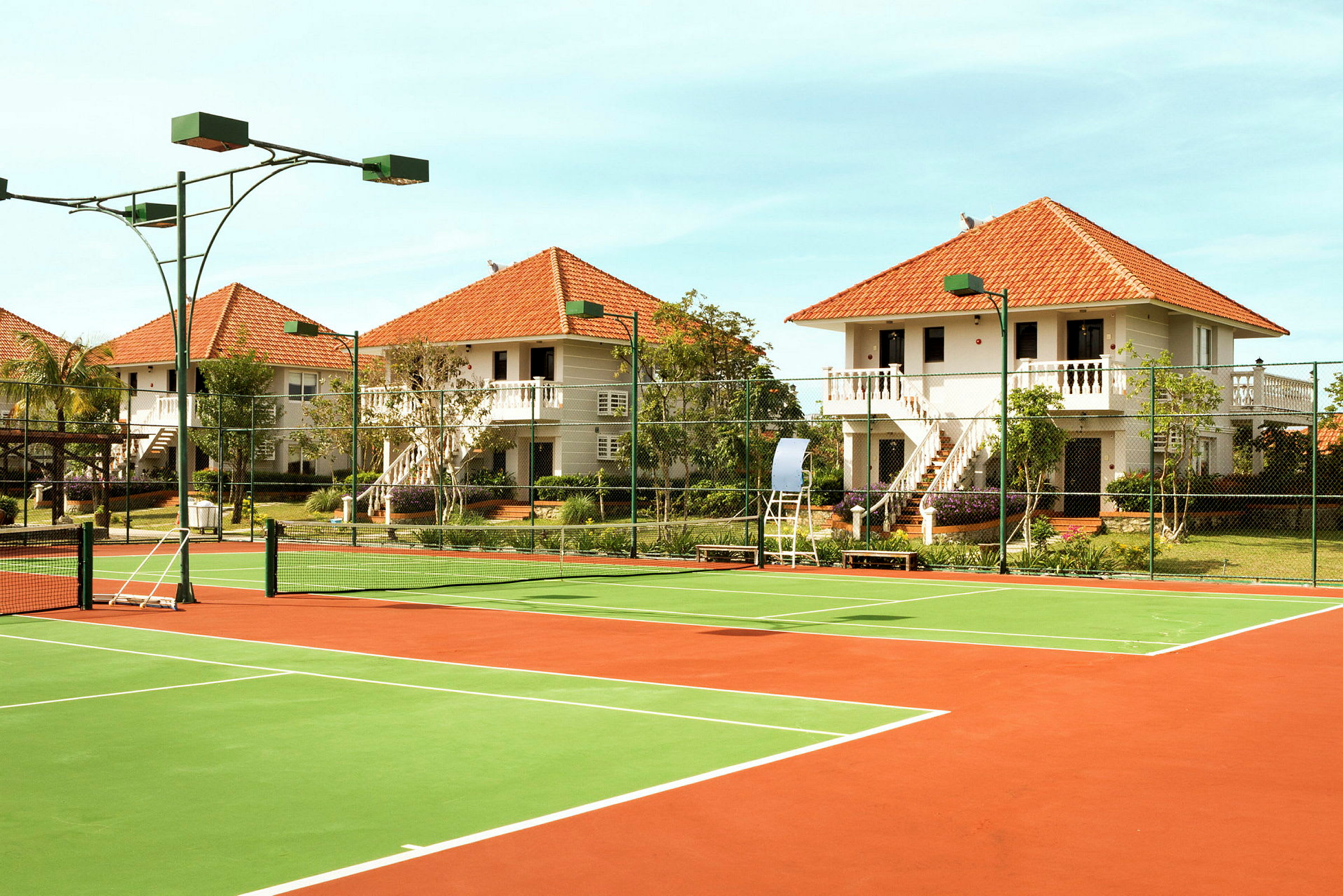 Bild av en tennisbana med grönt och rött underlag, omgiven av vissa flerbostadshus med röda tak. (AI-genererad text)