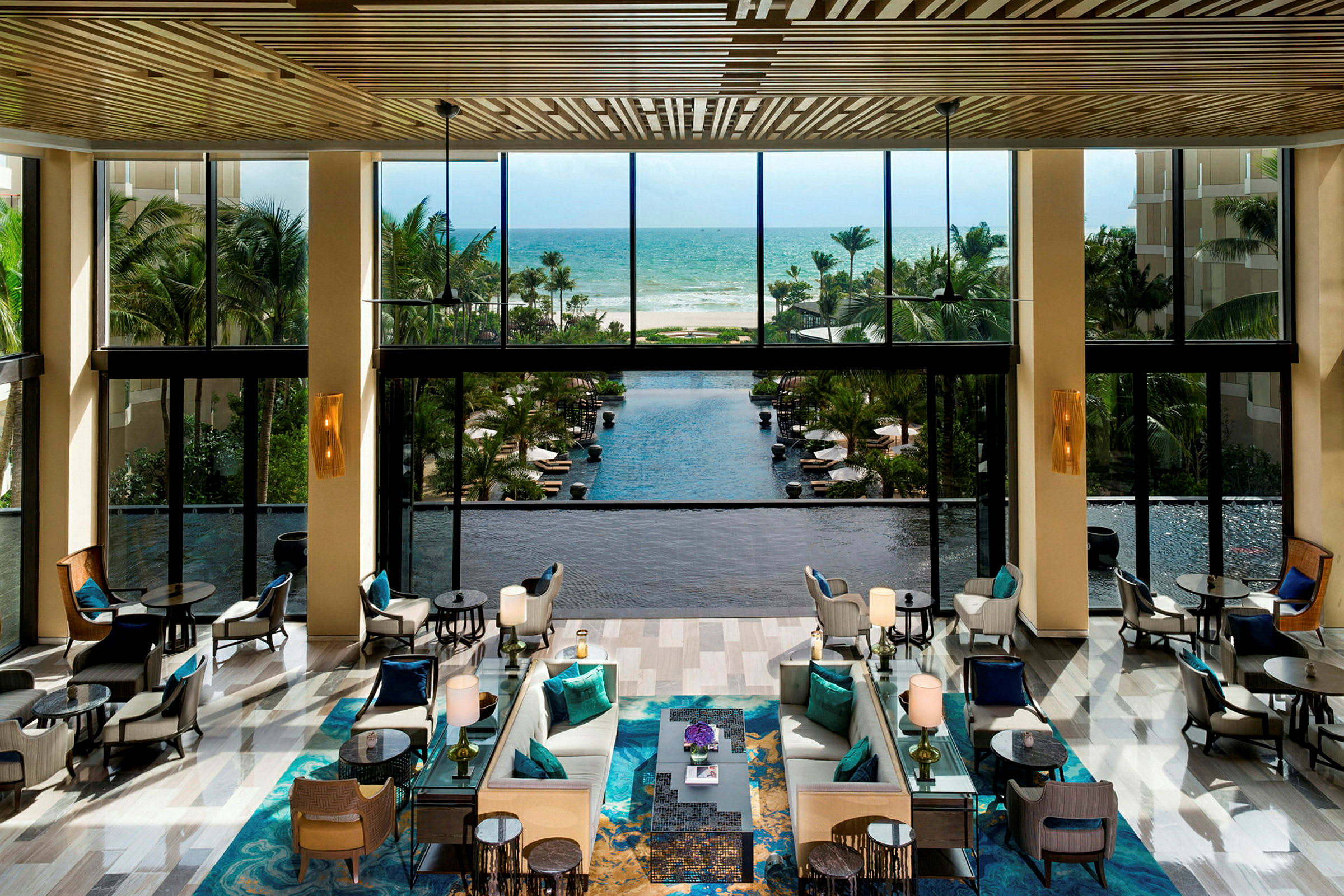 Hotellobby med sittgrupper, stora fönster som vetter mot en pool och havet i bakgrunden. (AI-genererad text)