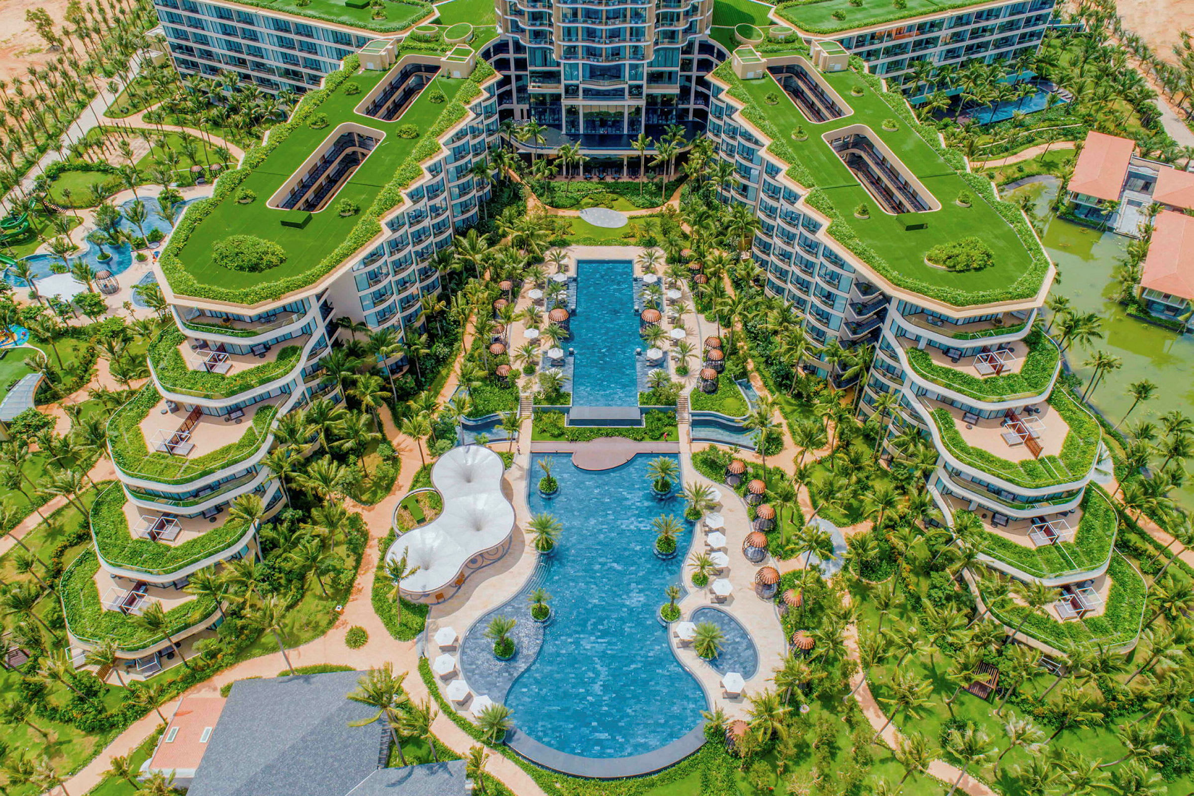 Flygbild av ett stort hotellkomplex med grönskande takterrasser och poolområden. (AI-genererad text)