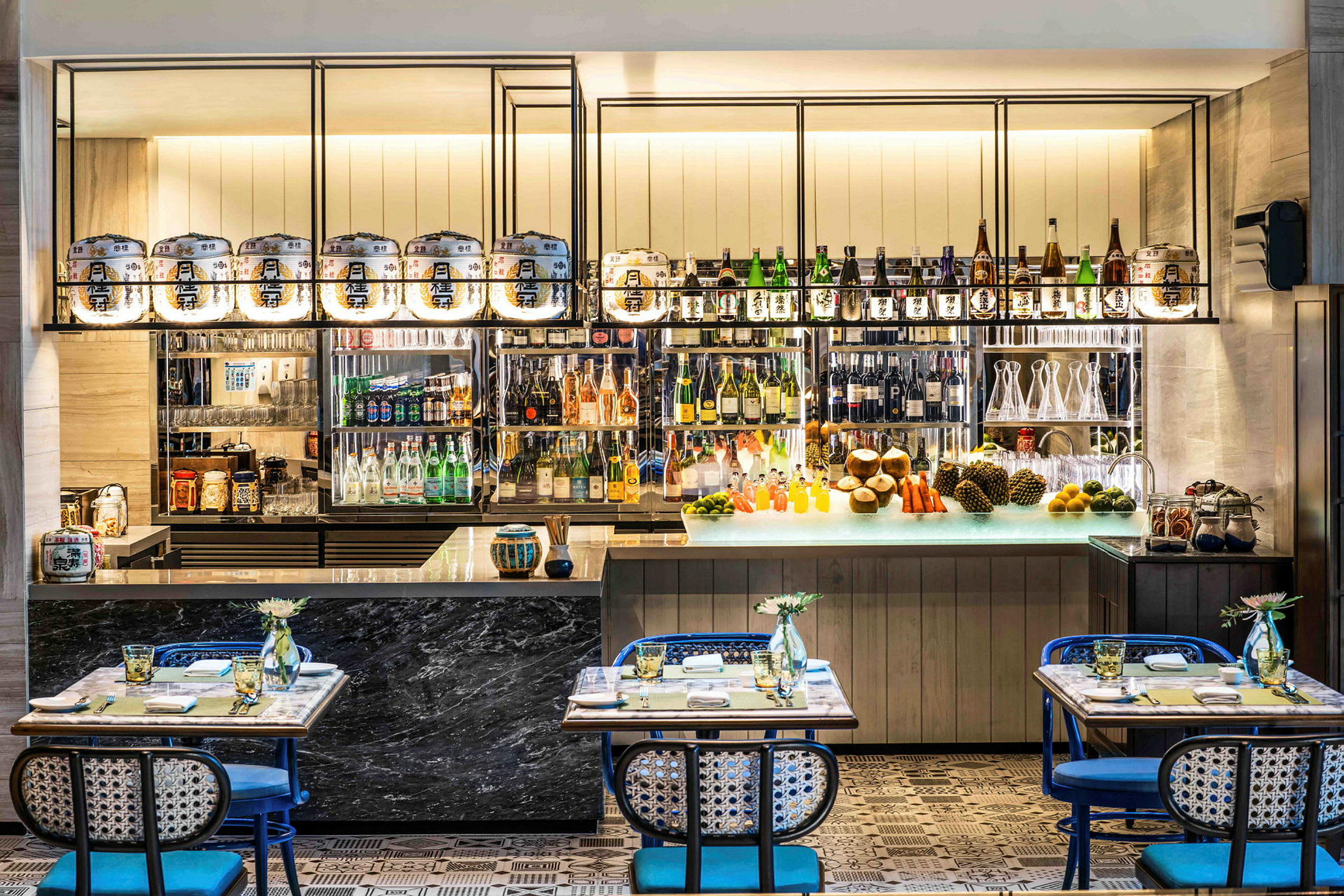 En stilfull bar med olika drycker på hyllorna samt bord och stolar i förgrunden. (AI-genererad text)