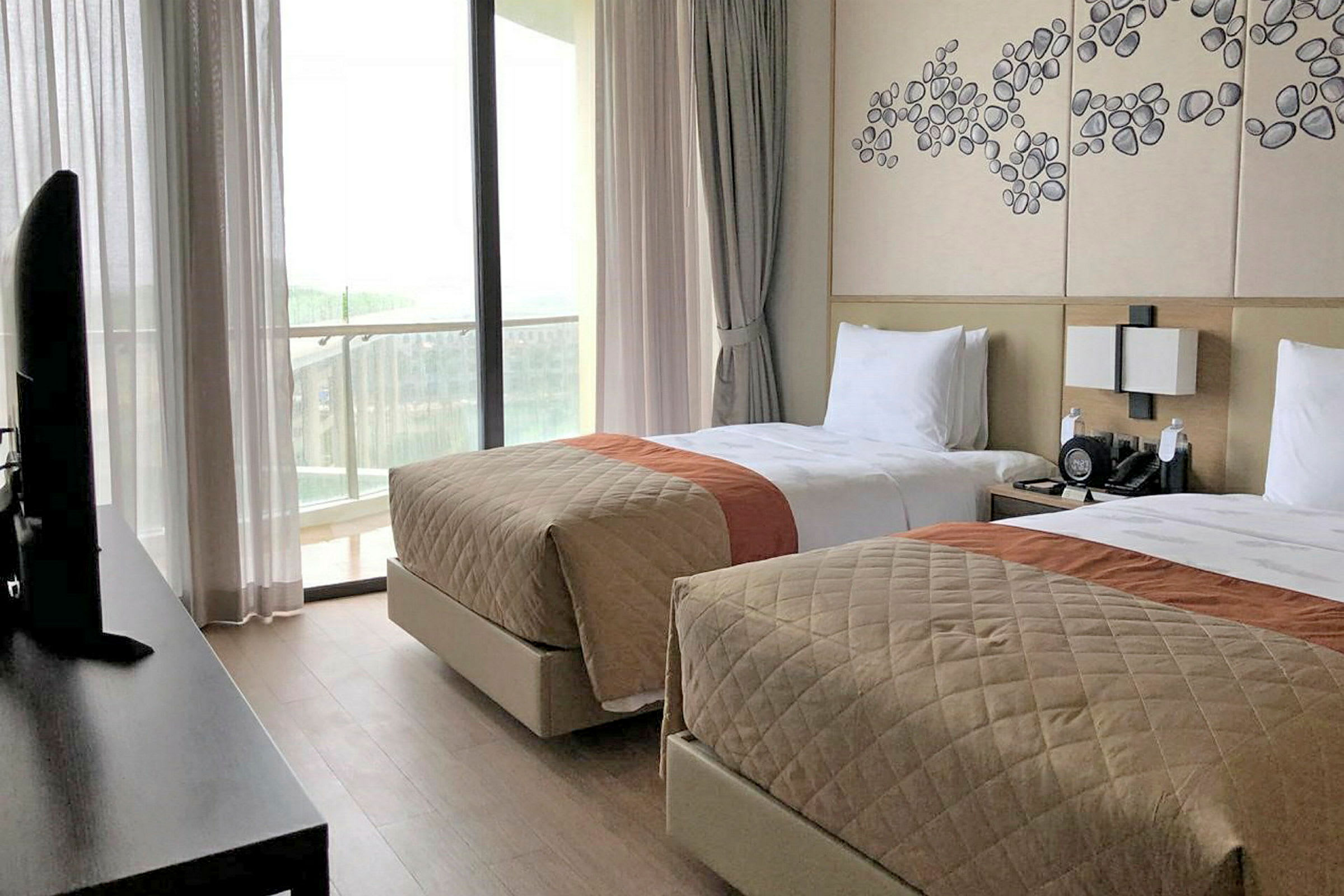 Hotellrum med två enkelsängar, en väggdekoration och utsikt mot en balkong med genomskinliga gardiner. (AI-genererad text)
