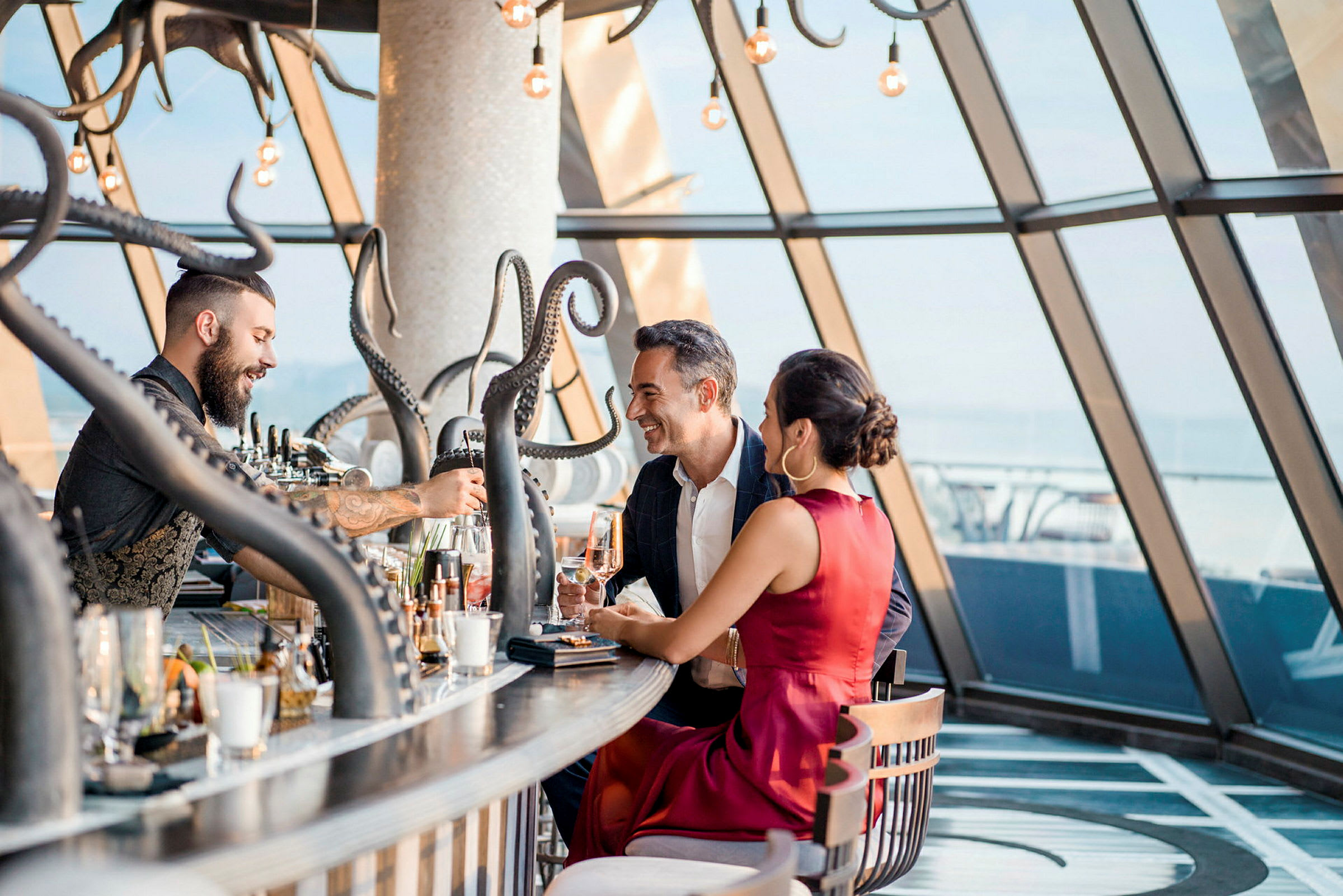 Ett par sitter vid en bar med tentakelliknande dekorationer och stora fönster som vetter mot utsikten utomhus. (AI-genererad text)