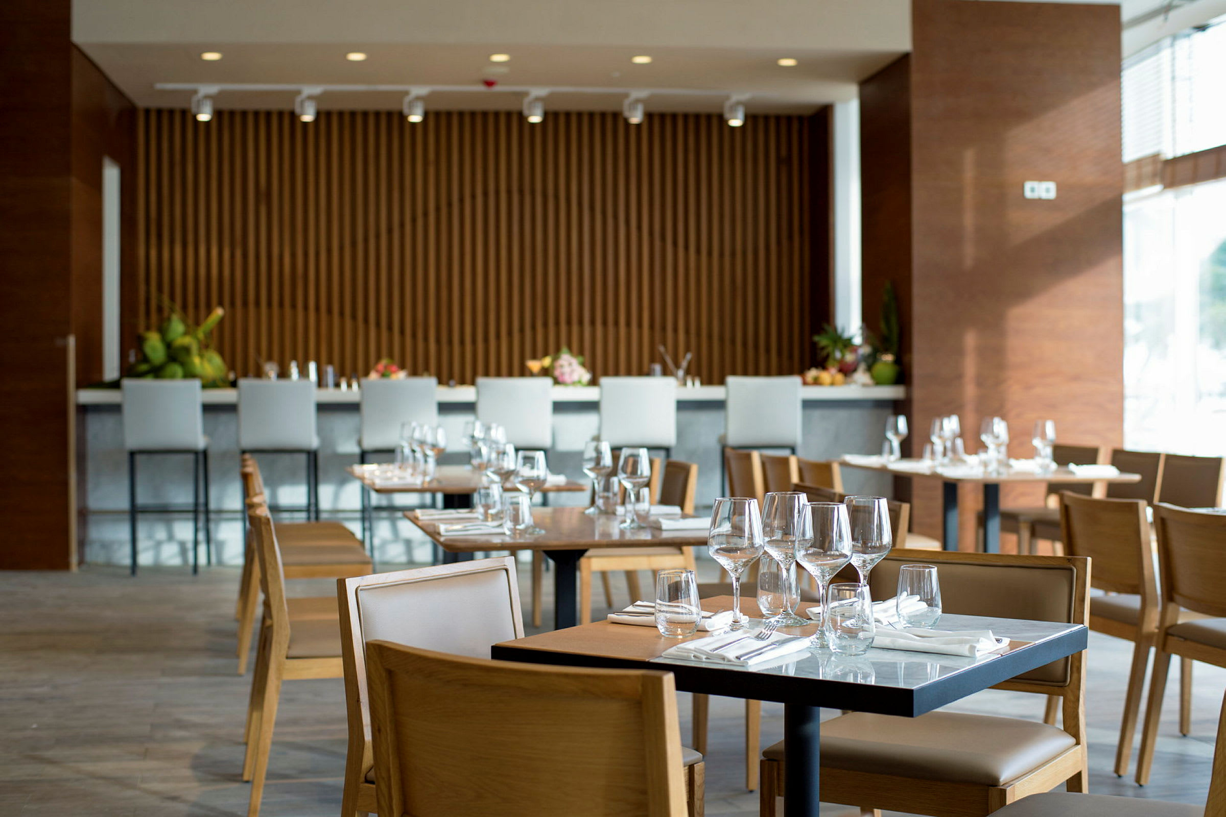 Ett modernt restaurangområde med träbord och stolar, dukat med glas och bestick. (AI-genererad text)